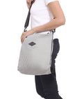 Close up view of a model facing the side. She is wearing a white tee shirt and black pants. She carries Sherpani mesh convertible bag, the Delanie, as a crossbody.