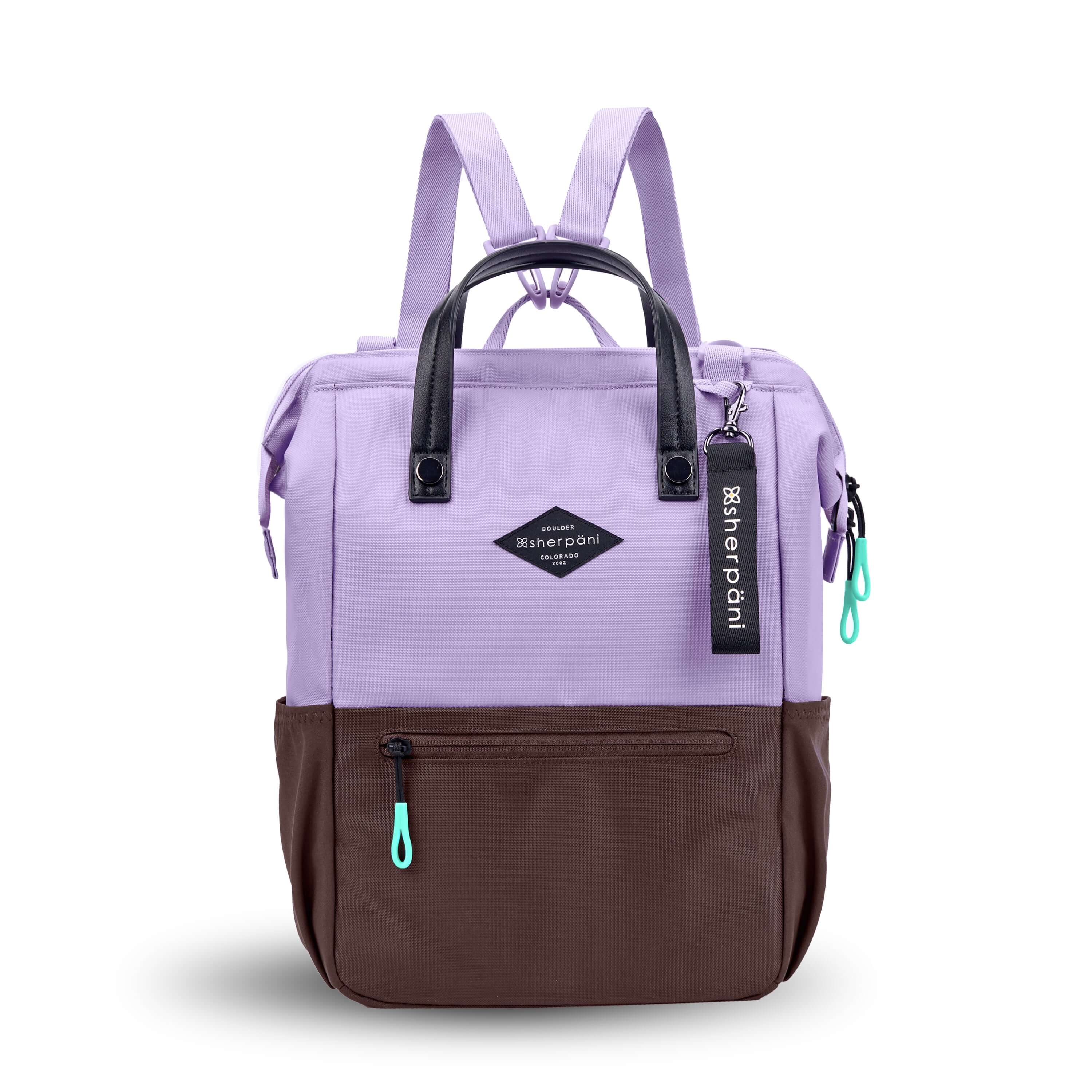 Flat front view of Sherpani three-in-one bag, the Dispatch in Lavender. The bag is two-toned: the top is lavender and the bottom is brown. There is an external zipper pocket on the front panel. Easy-pull zippers are accented in aqua. A branded Sherpani keychain is clipped to the upper right corner. Elastic water bottle holders sit on either side of the bag. It has short tote handles and adjustable/detachable straps that can function for a backpack or crossbody. 