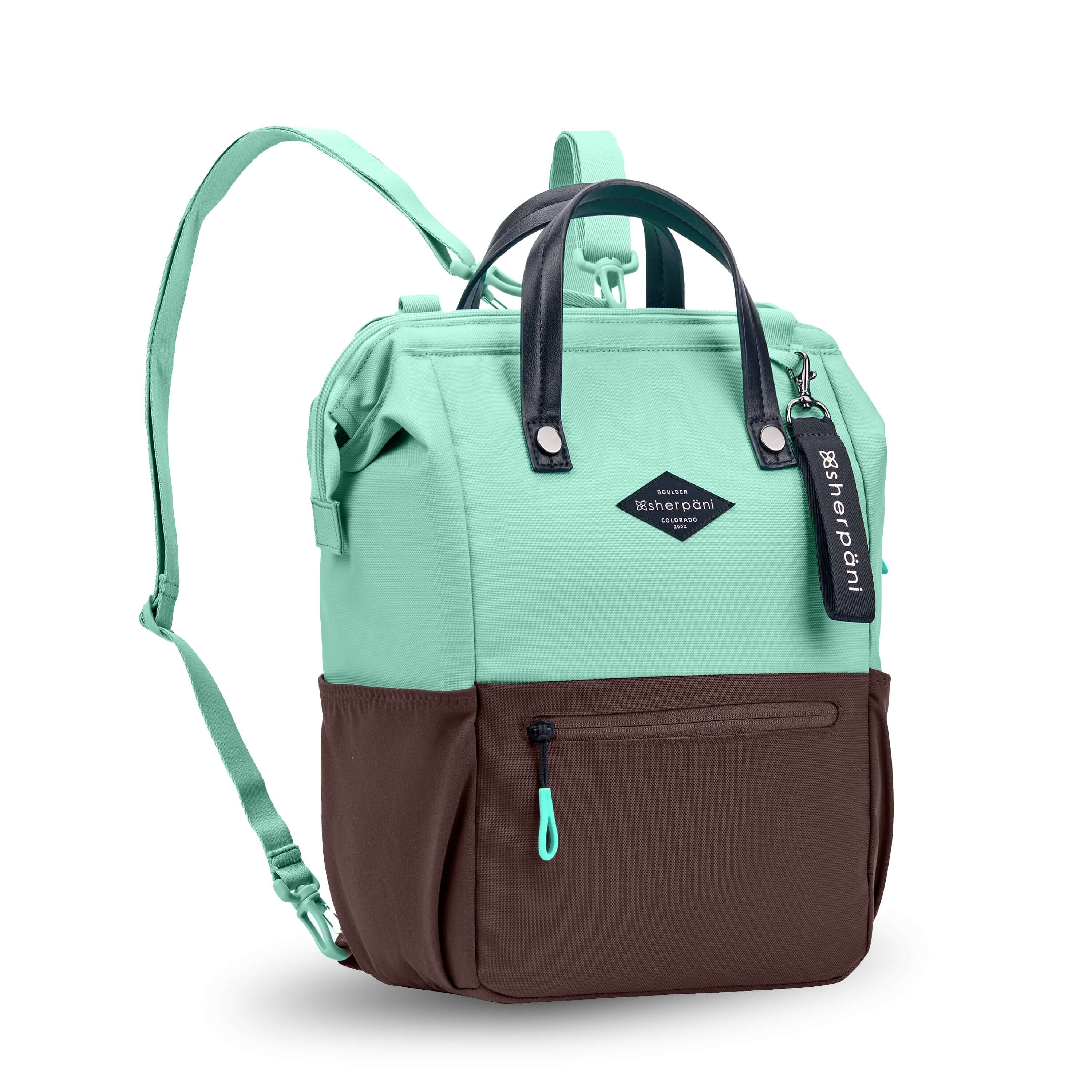 Angled front view of Sherpani three-in-one bag, the Dispatch in Seagreen. The bag is two-toned: the top is light green and the bottom is brown. There is an external zipper pocket on the front panel. Easy-pull zippers are accented in light green. A branded Sherpani keychain is clipped to the upper right corner. Elastic water bottle holders sit on either side of the bag. It has short tote handles and adjustable/detachable straps that can function for a backpack or crossbody. #color_seagreen