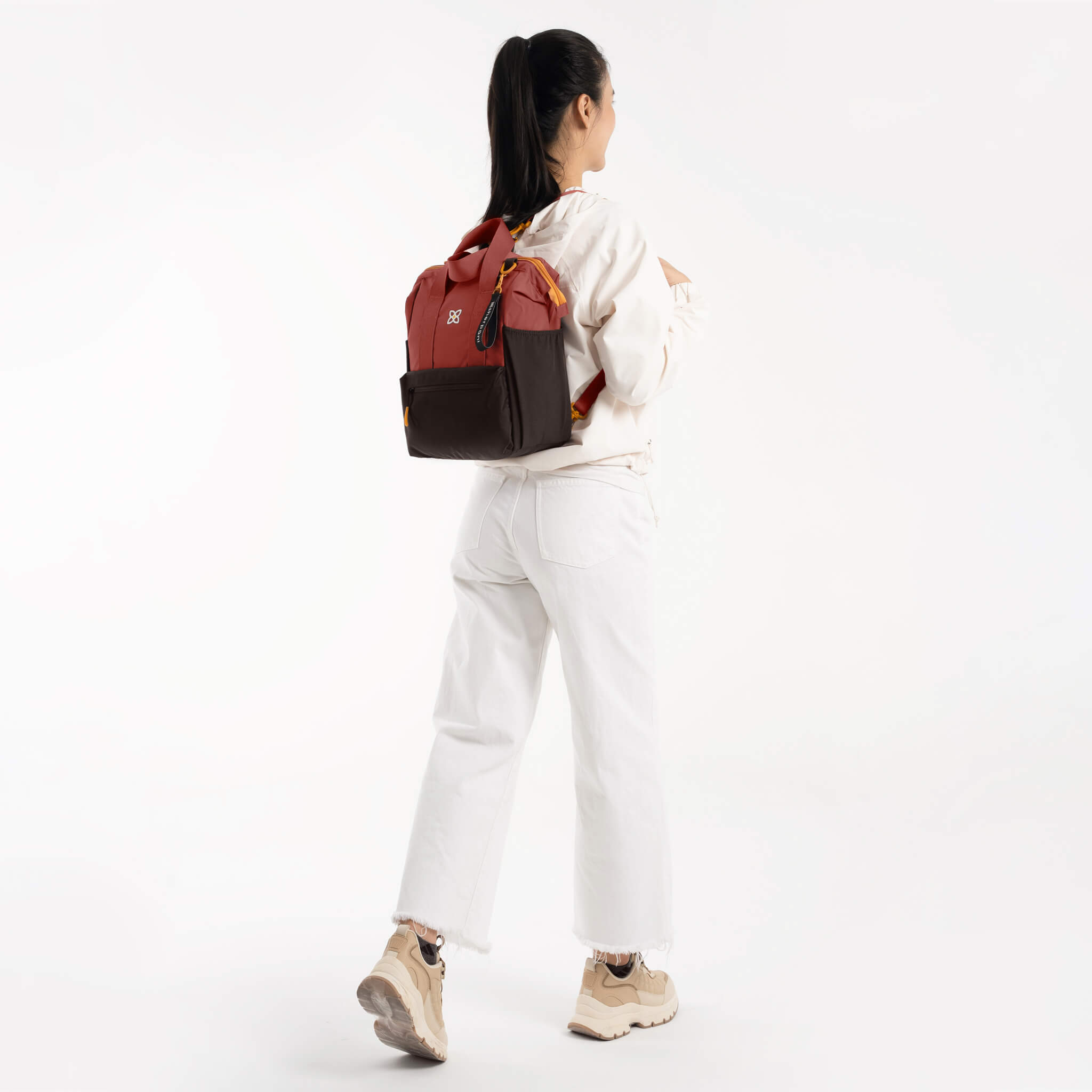 A model carrying Sherpani large travel purse, the Dispatch in Cider, with 3-in-one functionality as a tote bag, backpack and crossbody. 