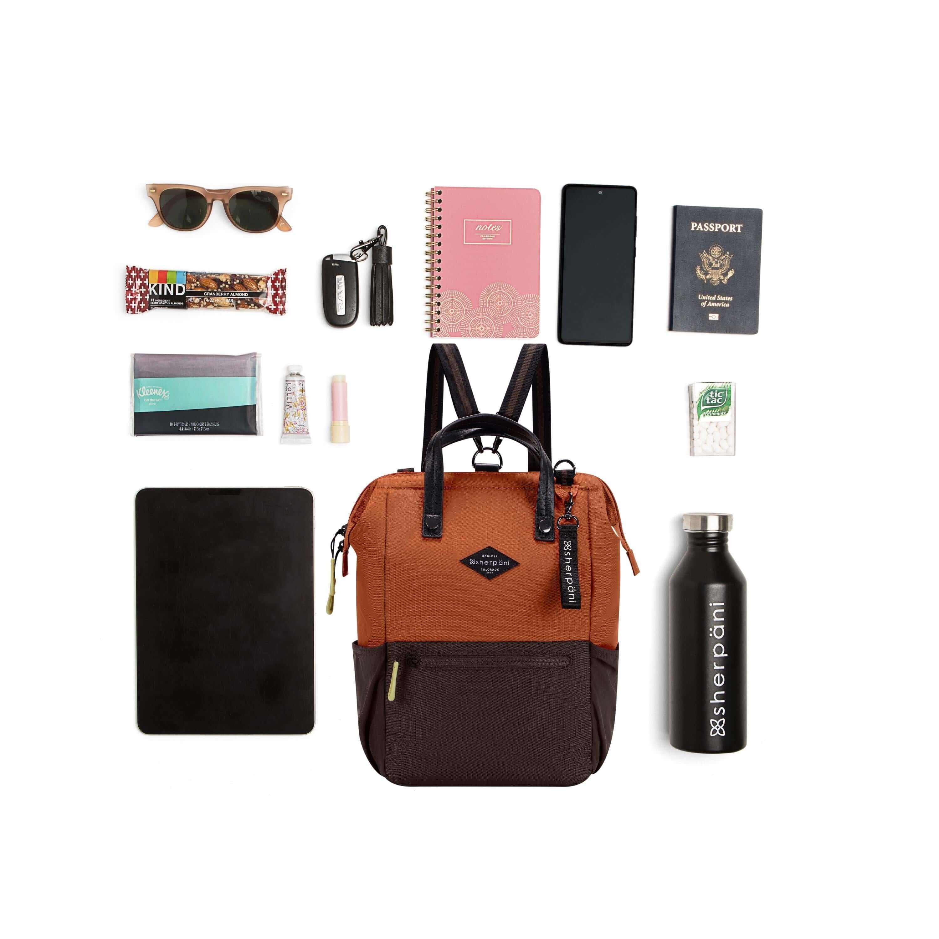 Top view of example items to fill the bag. Sherpani three-in-one bag, the Dispatch in Clay, lies in the center. It is surrounded by an assortment of items: sunglasses, granola bar, tissues, tablet, hand lotion, lip balm, car key, notebook, phone, passport, mints and water bottle. 