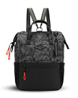 Flat front view of Sherpani three-in-one bag, the Dispatch in Dream Camo. The bag is two-toned: the top is a camouflage pattern of black and gray, and the bottom is black. There is an external zipper pocket on the front panel. Easy-pull zippers are accented in red. A branded Sherpani keychain is clipped to the upper right corner. Elastic water bottle holders sit on either side of the bag. It has short tote handles and adjustable/detachable straps that can function for a backpack or crossbody.