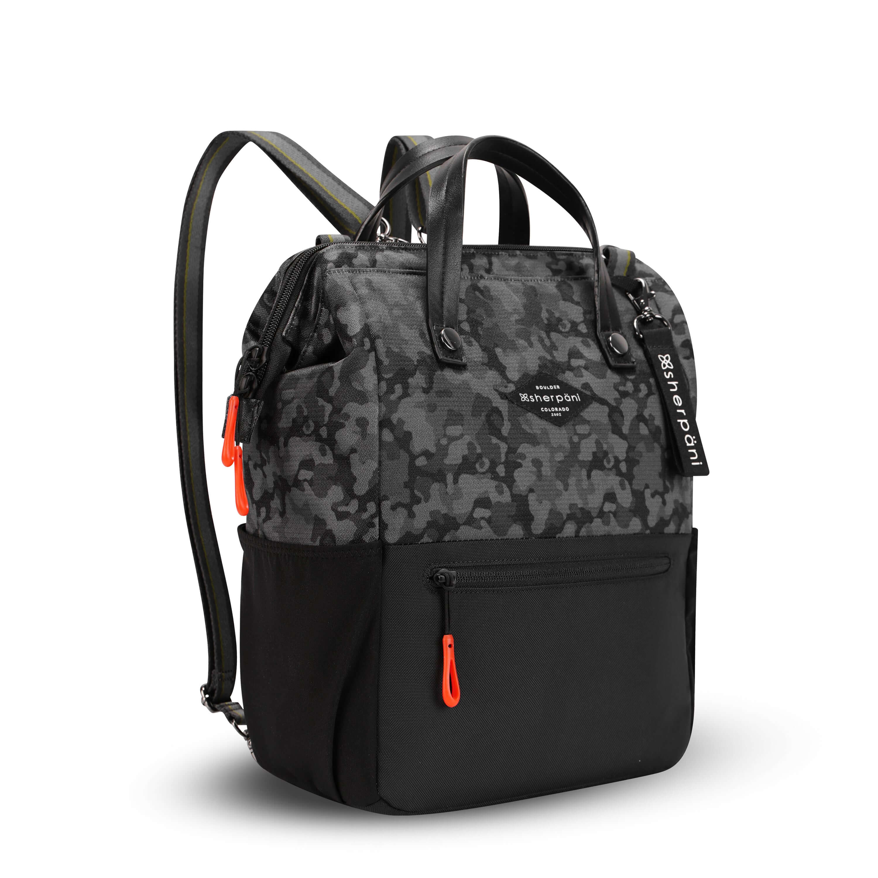 Angled front view of Sherpani three-in-one bag, the Dispatch in Dream Camo. The bag is two-toned: the top is a camouflage pattern of black and gray, and the bottom is black. There is an external zipper pocket on the front panel. Easy-pull zippers are accented in red. A branded Sherpani keychain is clipped to the upper right corner. Elastic water bottle holders sit on either side of the bag. It has short tote handles and adjustable/detachable straps that can function for a backpack or crossbody.