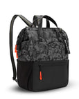 Angled front view of Sherpani three-in-one bag, the Dispatch in Dream Camo. The bag is two-toned: the top is a camouflage pattern of black and gray, and the bottom is black. There is an external zipper pocket on the front panel. Easy-pull zippers are accented in red. A branded Sherpani keychain is clipped to the upper right corner. Elastic water bottle holders sit on either side of the bag. It has short tote handles and adjustable/detachable straps that can function for a backpack or crossbody.