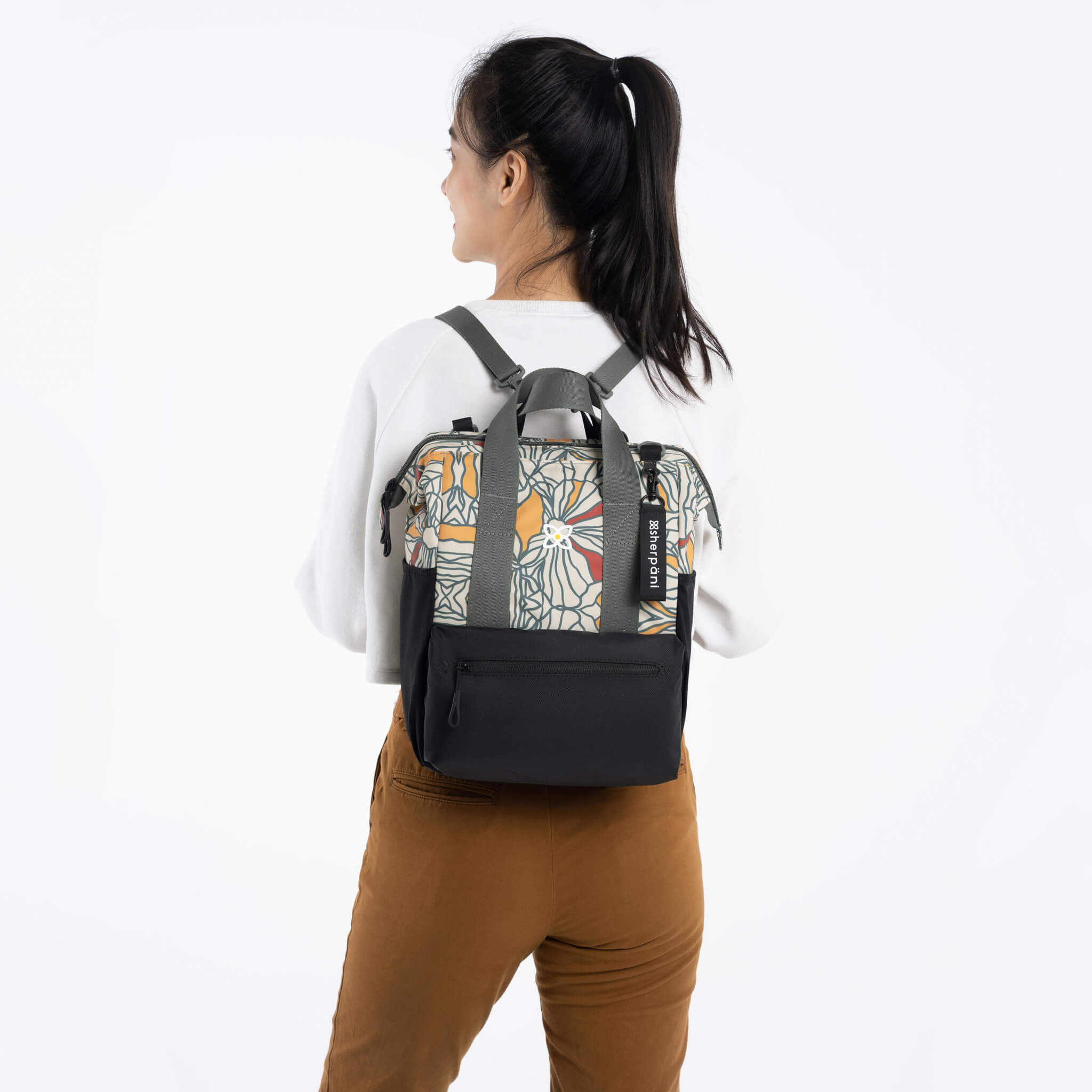 A model wearing Sherpani travel bag for women, the Dispatch in Fiori. She is using the removable straps to wear the Dispatch as a backpack. 