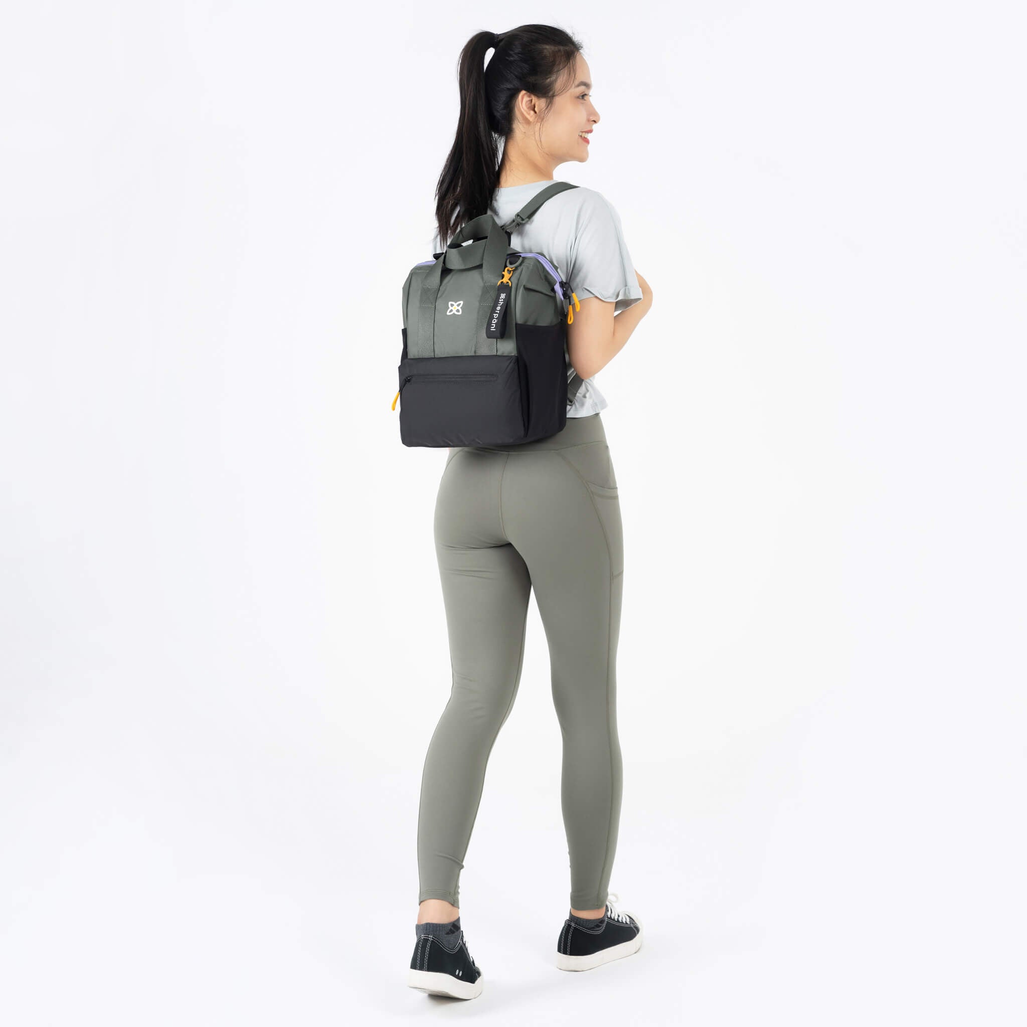 A model showing Sherpani multifunctional travel bag, the Dispatch in Juniper, as a backpack with adjustable and comfortable backpack straps. 