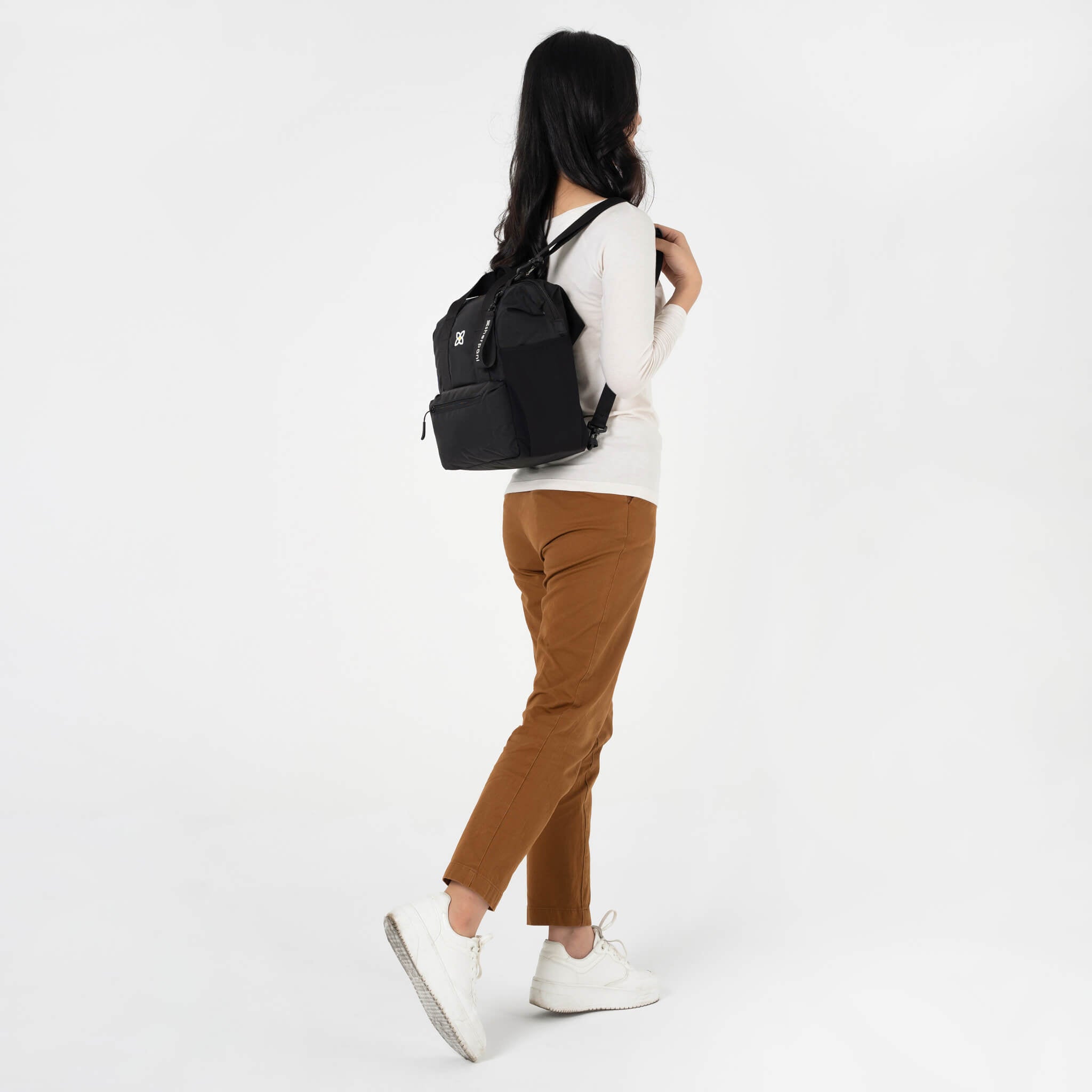 A model showing Sherpani travel purse for women, the Dispatch in Raven. She is wearing the travel bag as a backpack with the detachable backpack straps. 