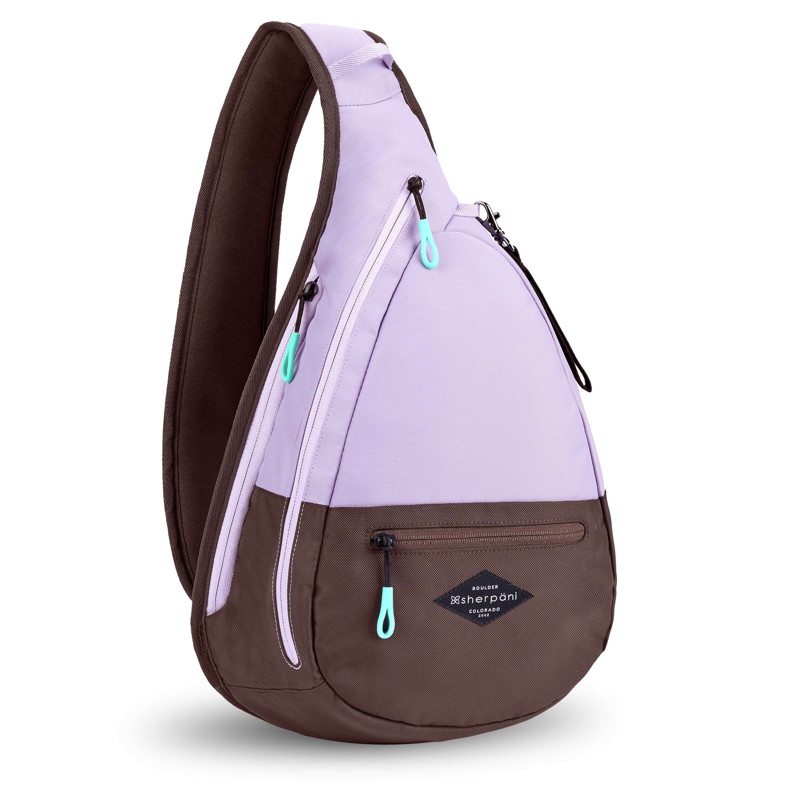 Angled front view of Sherpani's bag, the Esprit in Lavender. The teardrop shaped bag is two-toned in lavender and brown. There is a small zipper pocket on the front of the bag, the main zipper compartment in the middle, and another zipper pocket towards the back of the bag. It has easy-pull zippers accented in aqua. A branded Sherpani keychain is clipped to a fabric loop near the top of the bag. 