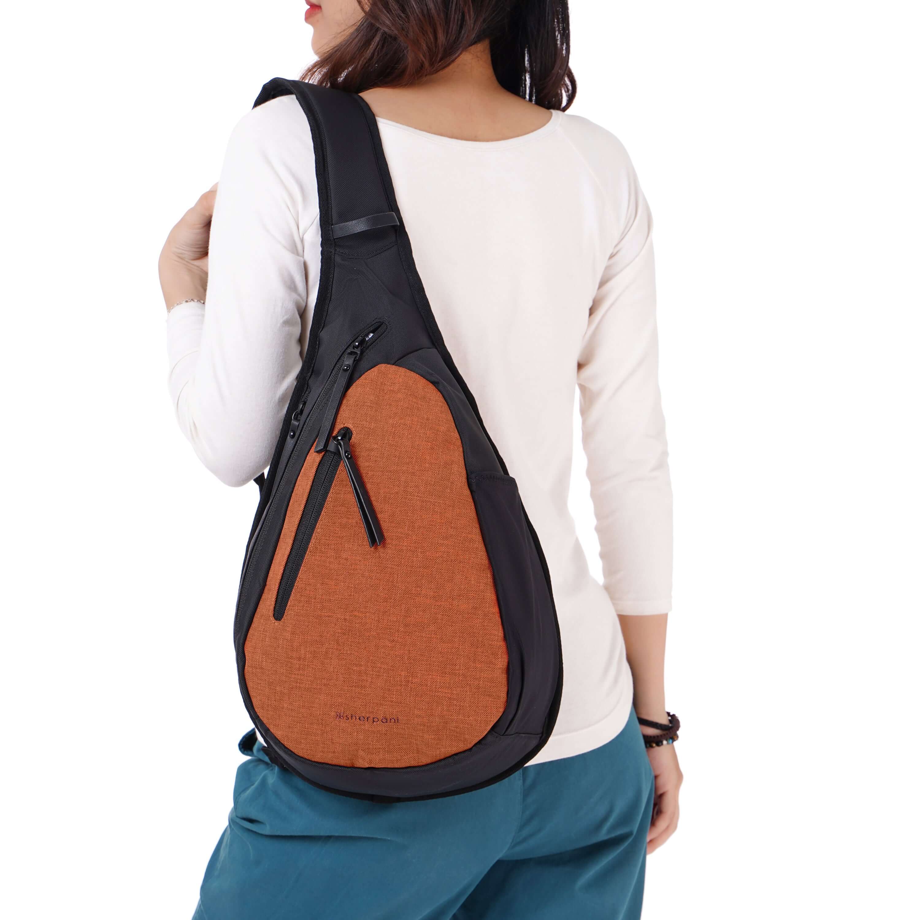 Close up view of a dark haired model facing away from the camera. She is wearing a white shirt, blue pants and Sherpani’s Anti-Theft bag, the Esprit AT in Copper, over her shoulder.