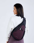 Close up view of a dark haired model facing away from the camera and smiling over her left shoulder. She is wearing a white sweatshirt, purple leggings and Sherpani’s Anti-Theft bag, the Esprit AT in Merlot, across her body.