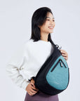 Close up view of a dark haired model facing the camera and smiling. She is wearing a white sweatshirt, purple leggings and Sherpani’s Anti-Theft bag, the Esprit AT in Teal, as a crossbody.