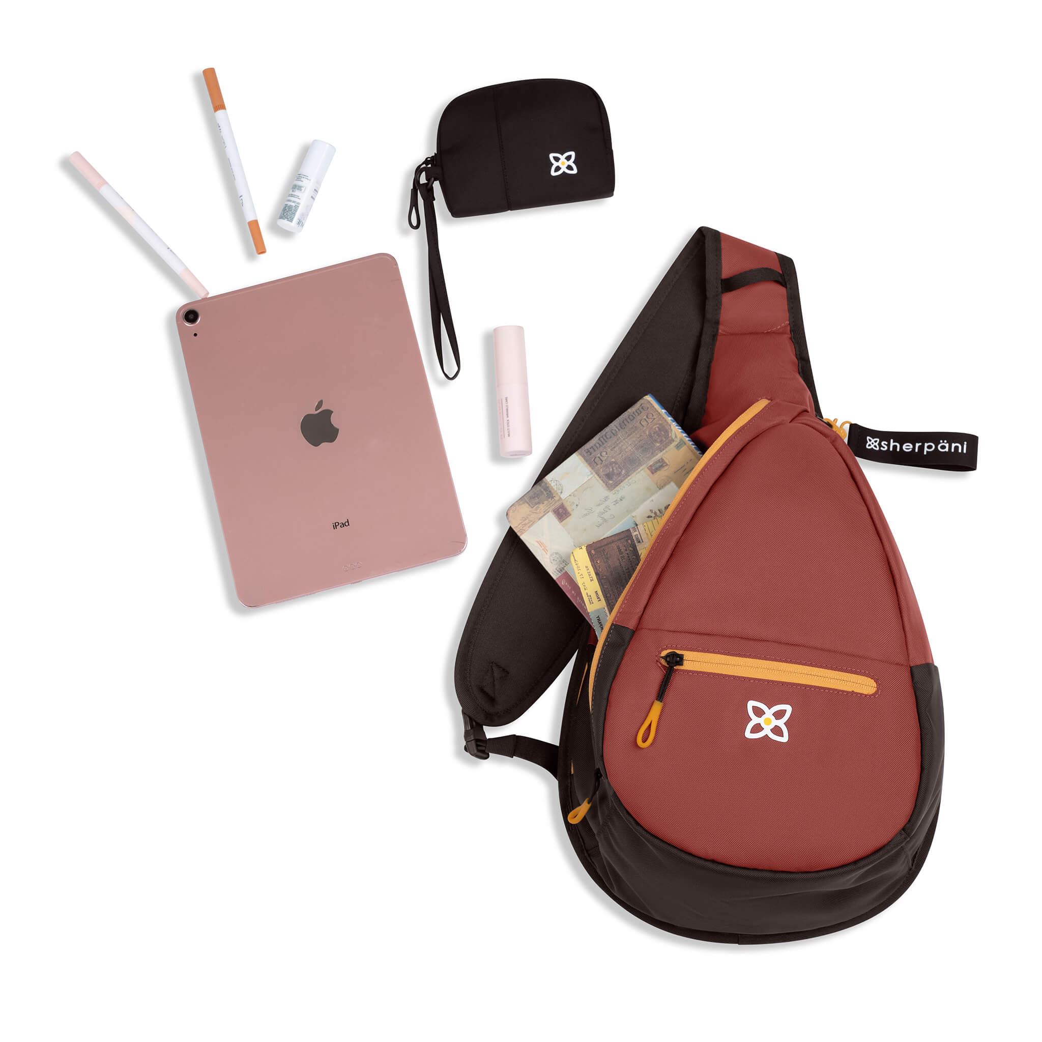 Top view of Sherpani women&#39;s sling bag, the Esprit in Cider. It is surrounded by example travel accessories to pack inside.