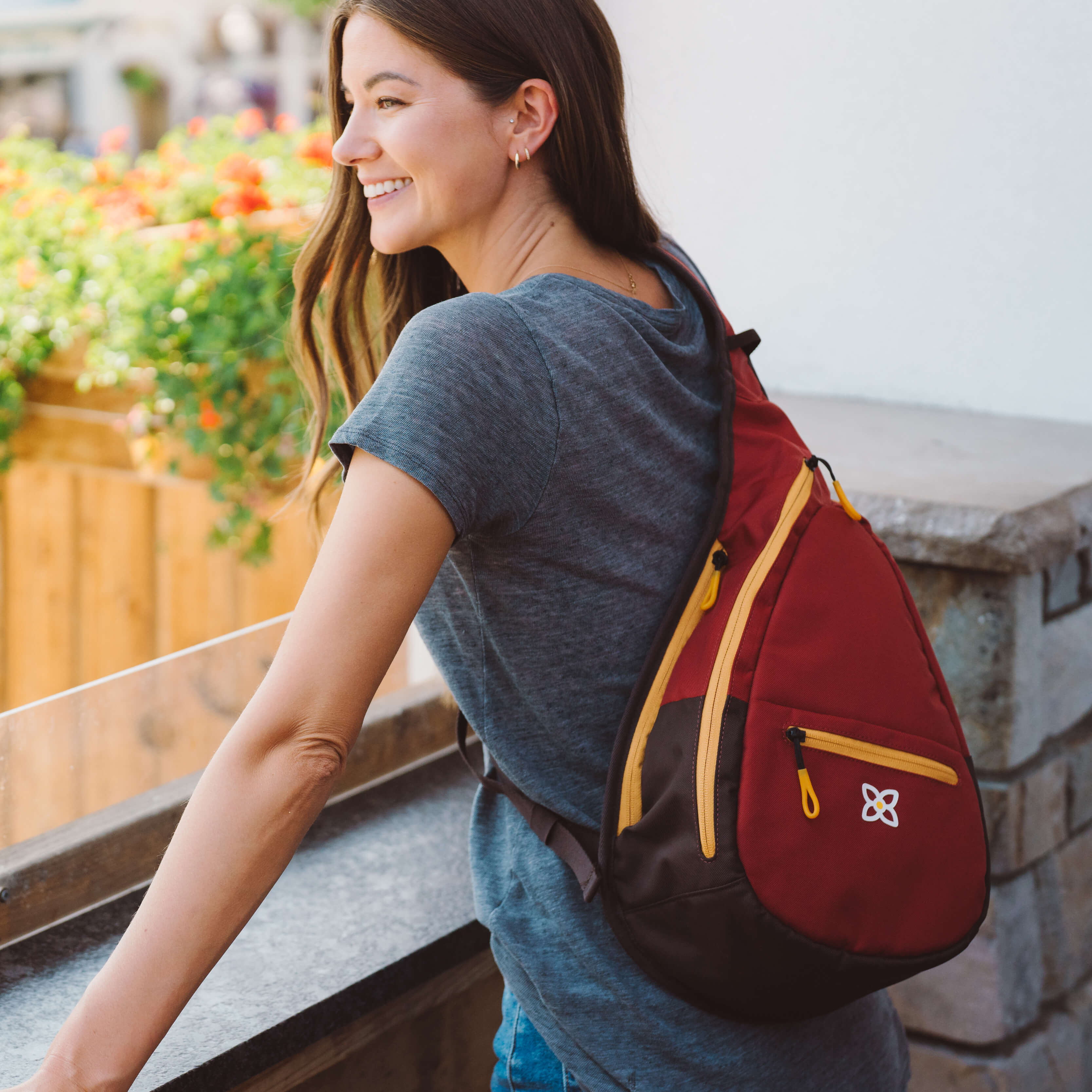 A woman leaning on a a balcony outside. She is wearing Sherpani travel sling backpack, the Esprit in Cider.