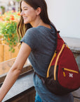 A woman leaning on a a balcony outside. She is wearing Sherpani travel sling backpack, the Esprit in Cider.