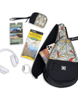 Top view of Sherpani women's sling bag, the Esprit in Fiori. It is surrounded by example travel accessories such as travel guides and a travel map to pack inside.