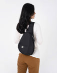 A model wearing the Esprit in Raven, a sling style backpack built for women's travel.