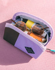 Top view of Sherpani travel accessory, the Harmony in Lavender. The pouch is open to reveal several items: sunglasses, granola bar and sunscreen.