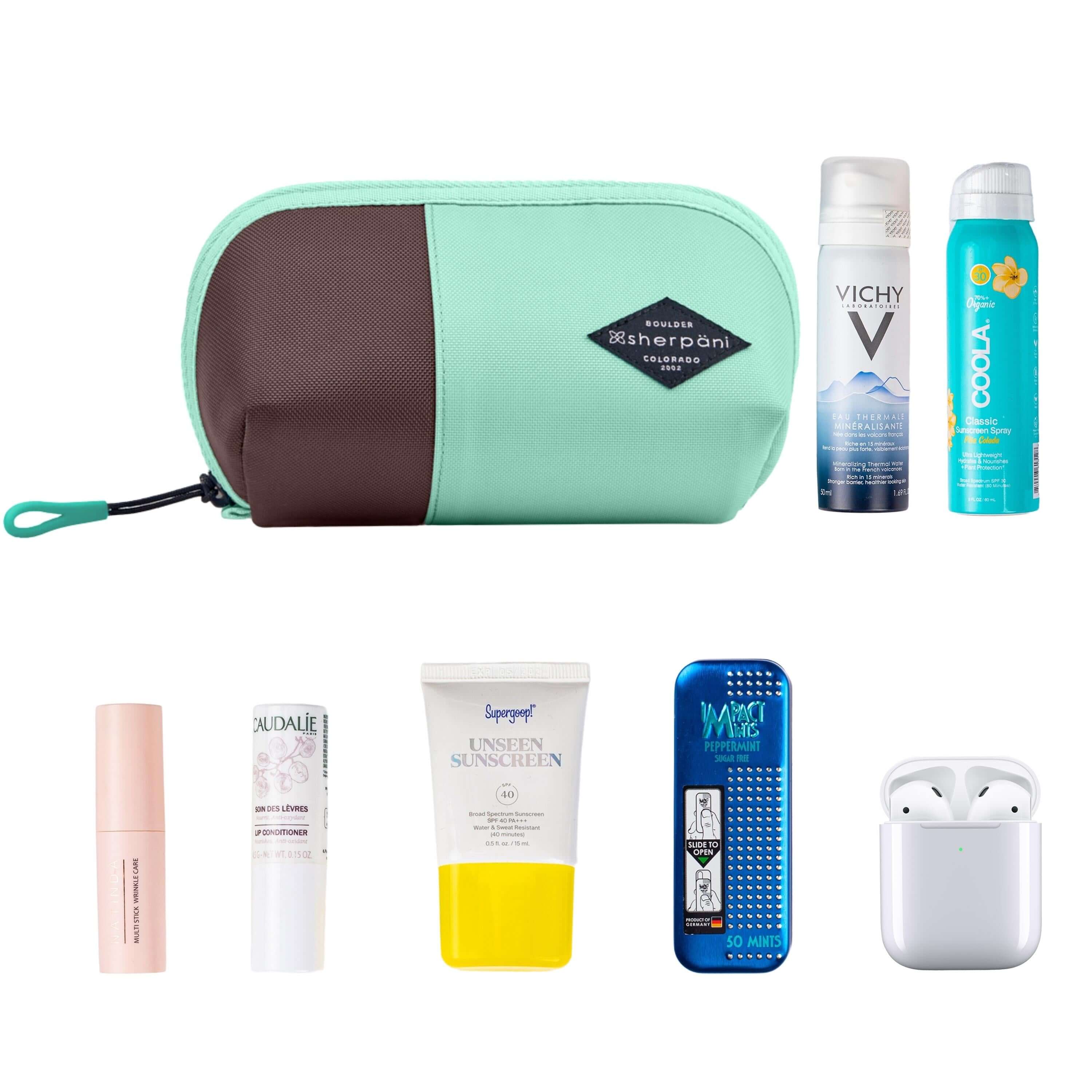 Top view of example items to fill the bag. Sherpani travel accessory, the Harmony in Seagreen, is shown in the upper left corner. It is surrounded by an assortment of items: beauty products, skincare products, sunscreen, mints and AirPods. 