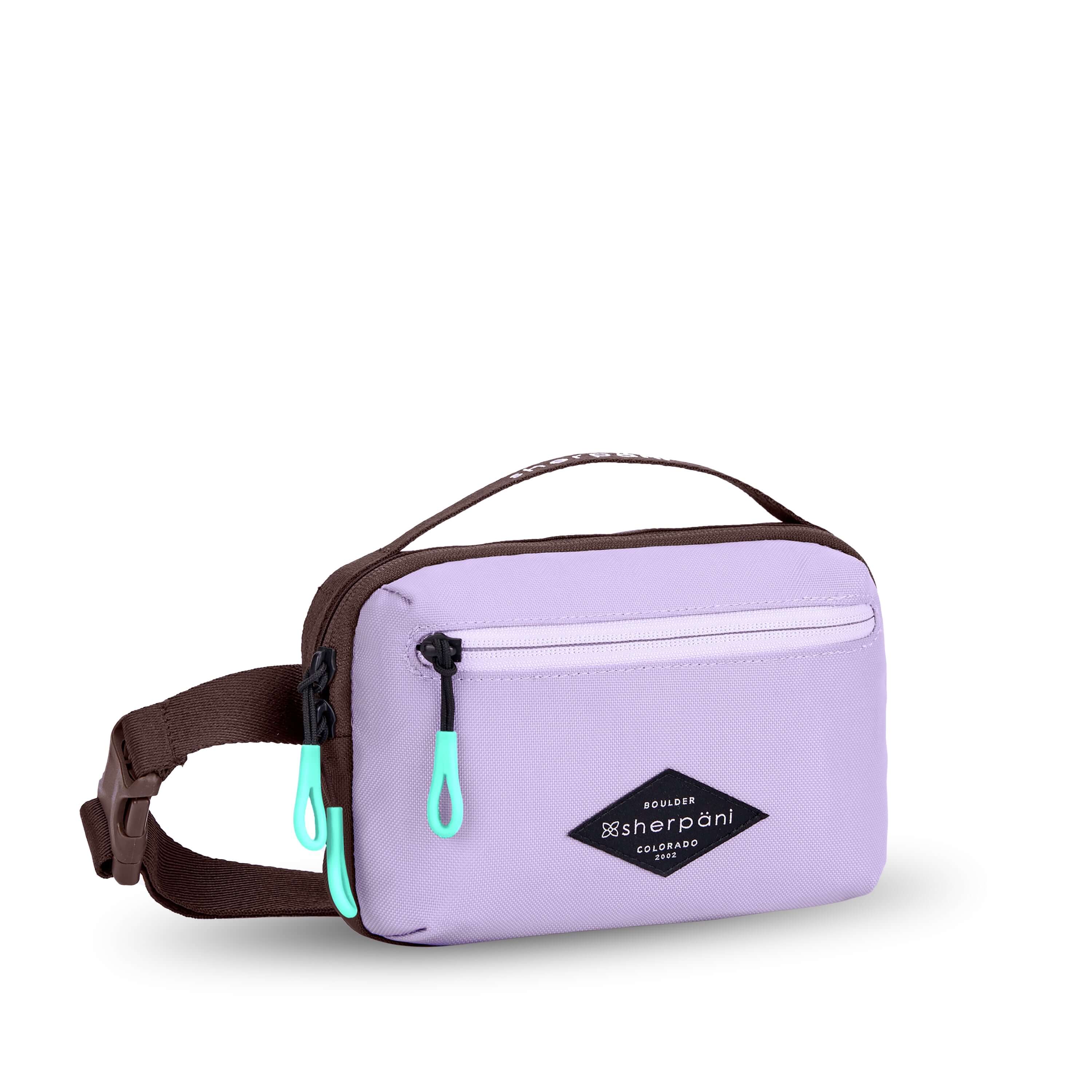 Angled front view of Sherpani’s fanny pack, the Hyk in Lavender. The bag is two-toned, the front half is lavender and the back half is brown. There is an external zipper pocket on the front of the bag. Easy-pull zippers are accented in aqua. The fanny pack features an adjustable strap with a buckle.