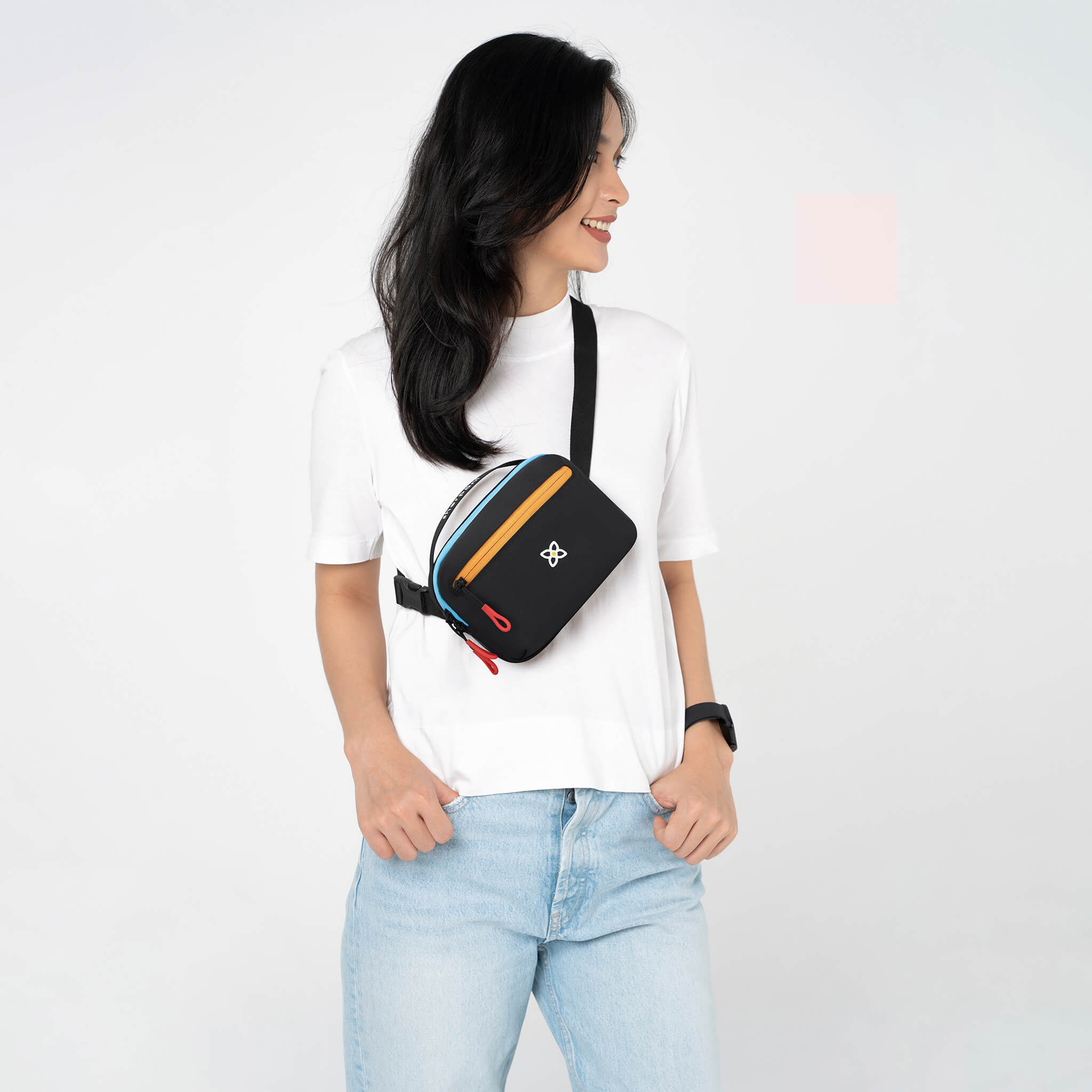 Close up view of a dark haired model smiling over her right shoulder. She is wearing a white tee shirt, faded jeans and Sherpani&#39;s fanny pack, the Hyk in Chromatic, as a crossbody