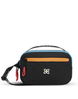 Flat front view of Sherpani’s fanny pack, the Hyk in Chromatic. The bag is black with yellow and blue accents. There is an external zipper pocket on the front of the bag. Easy-pull zippers are accented in red. The fanny pack features an adjustable strap with a buckle.