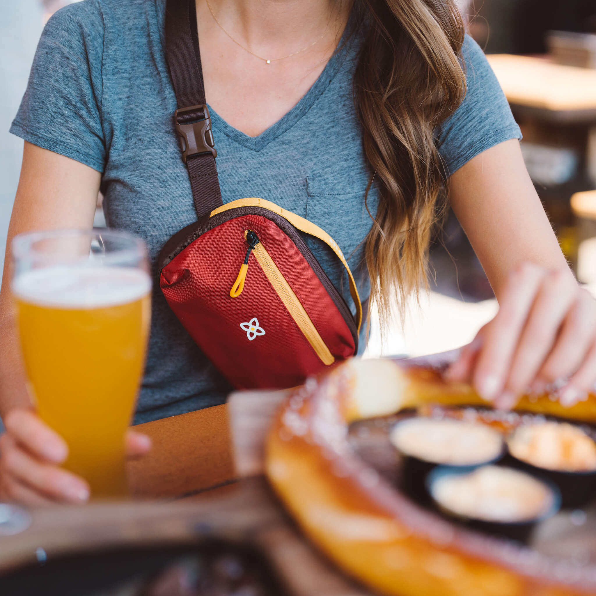 A woman dining is wearing Sherpani travel belt bag, the Hyk in Cider, as a crossbody purse. 