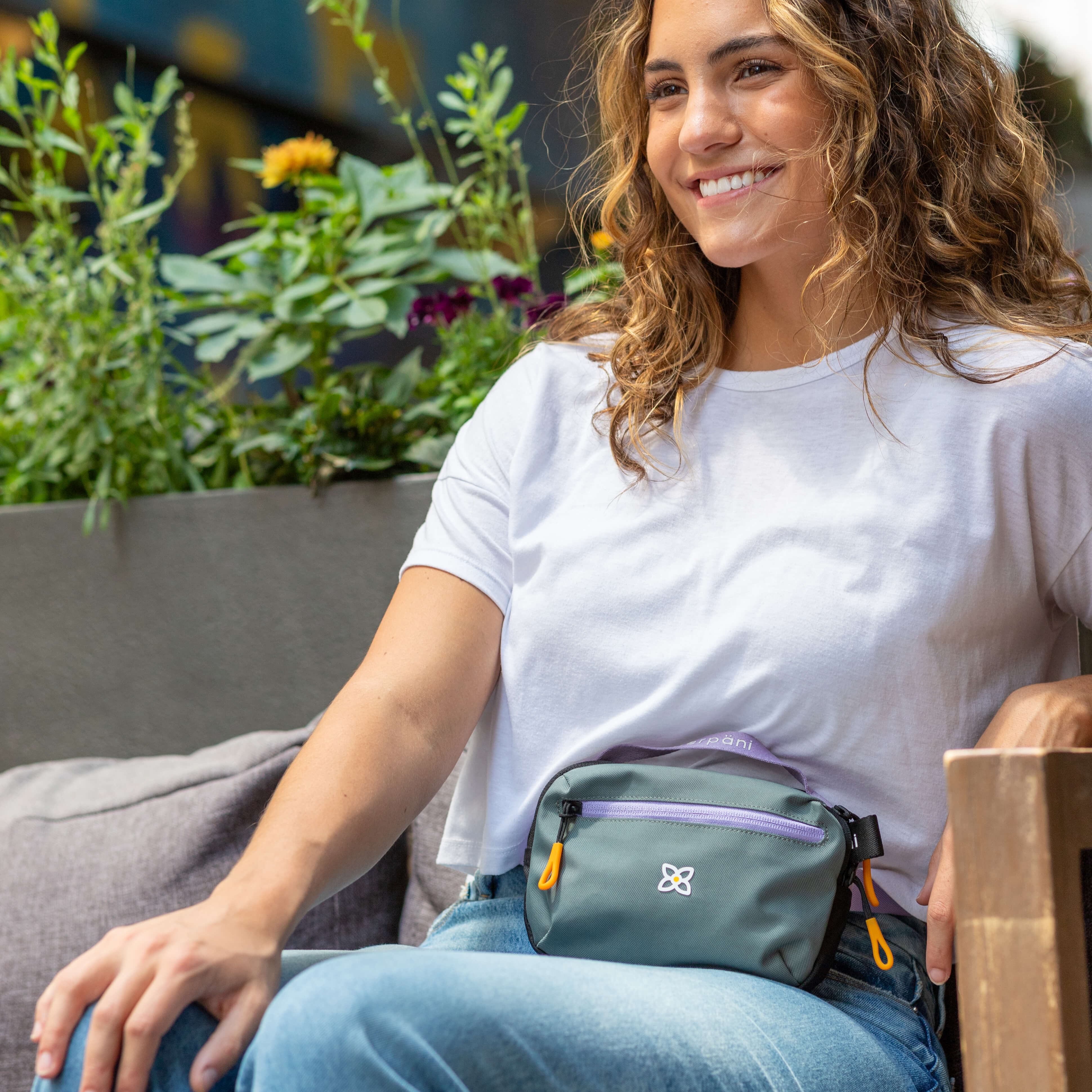 A woman sitting outside is wearing Sherpani travel fanny pack, the Hyk in Moonstone, as a belt bag.