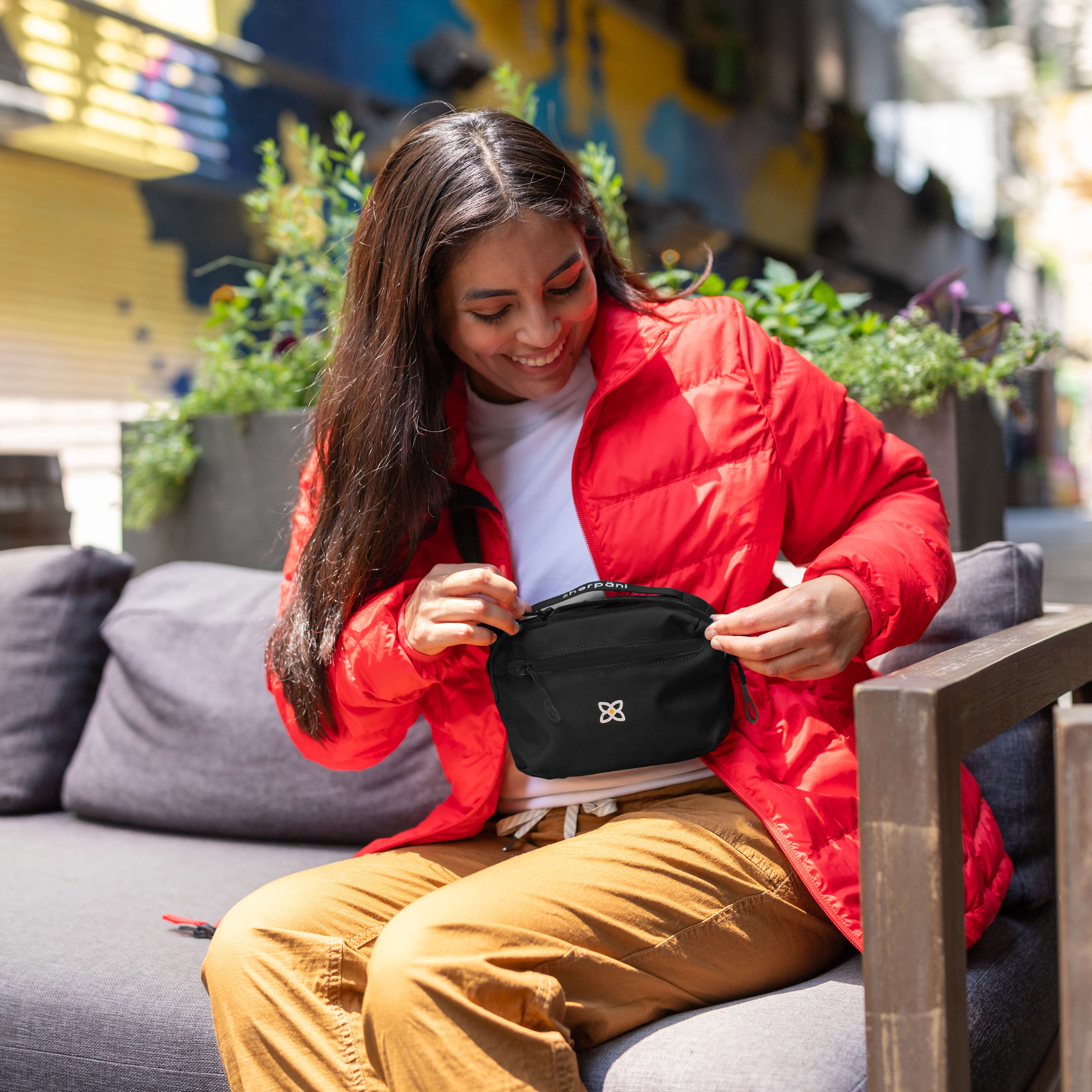 A woman sitting outside wearing Sherpani travel hip pack, the Hyk in Raven, as a mini crossbody bag.