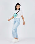 Full body view of a dark haired model smiling over her left shoulder. She is wearing a white tee shirt, faded jeans, white shoes and Sherpani's fanny pack, the Hyk in Seagreen, as a crossbody.