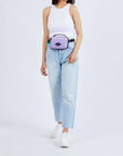 Close up view of a dark haired model. She is wearing a white tank top, jeans, white sneakers, and Sherpani's fanny pack, the Hyk in Lavender, as a fanny pack.