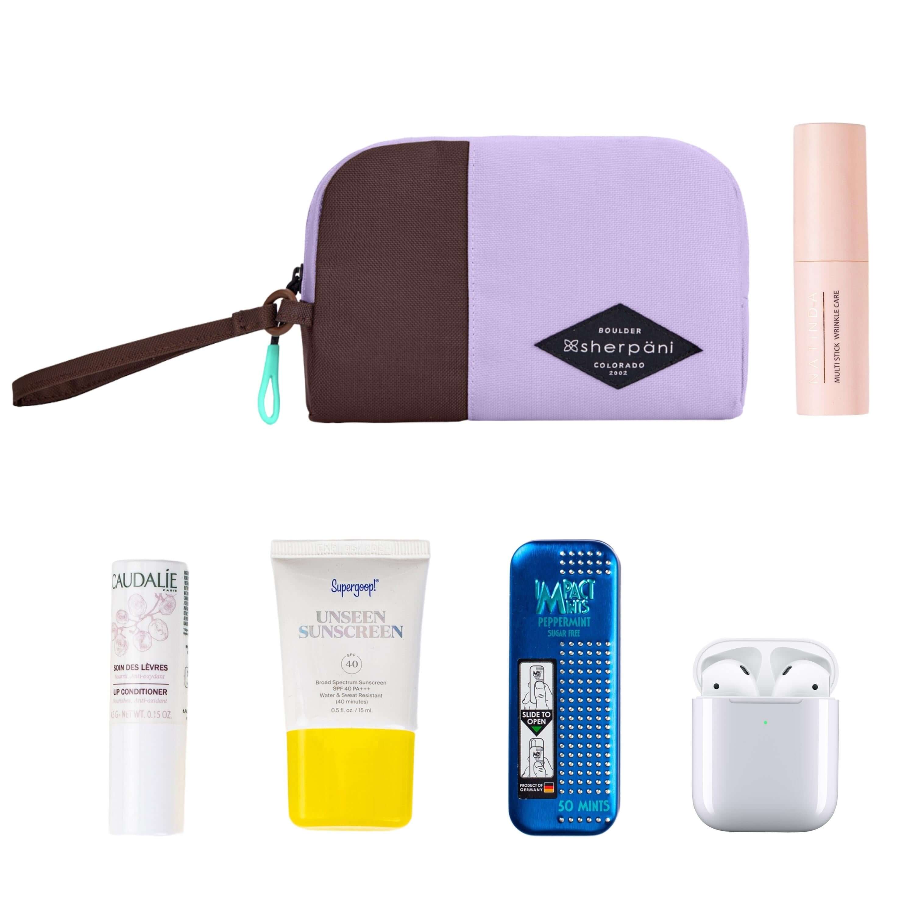 Top view of example items to fill the bag. Sherpani travel accessory, the Jolie in Lavender in small size, lies in the upper left corner. It is surrounded by an assortment of items: beauty product, skincare product, sunscreen, mints and AirPods.