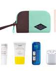 Top view of example items to fill the bag. Sherpani travel accessory, the Jolie in Seagreen in small size, lies in the upper left corner. It is surrounded by an assortment of items: beauty product, skincare product, sunscreen, mints and AirPods.