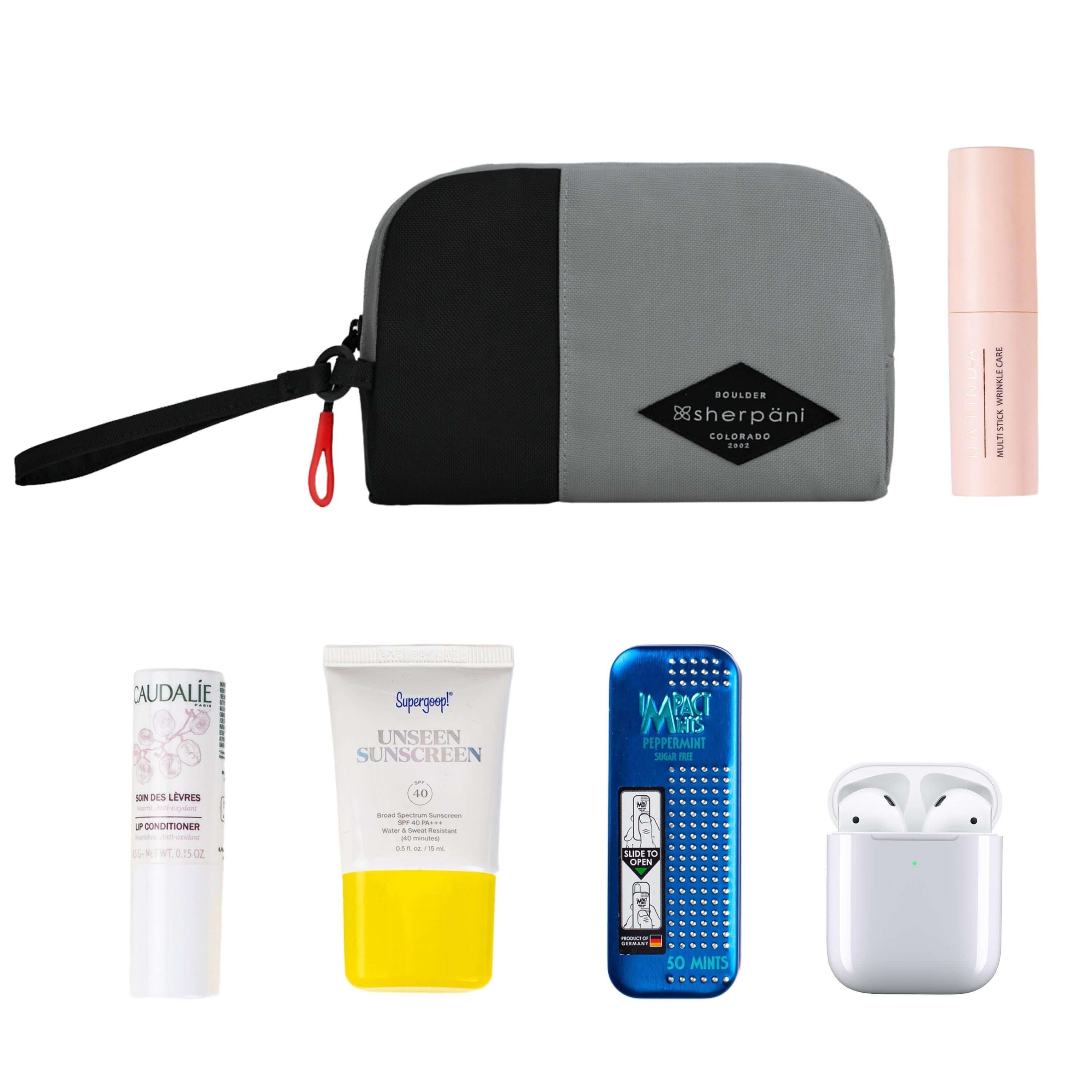 Top view of example items to fill the bag. Sherpani travel accessory, the Jolie in Stone in small size, lies in the upper left corner. It is surrounded by an assortment of items: beauty product, skincare product, sunscreen, mints and AirPods.