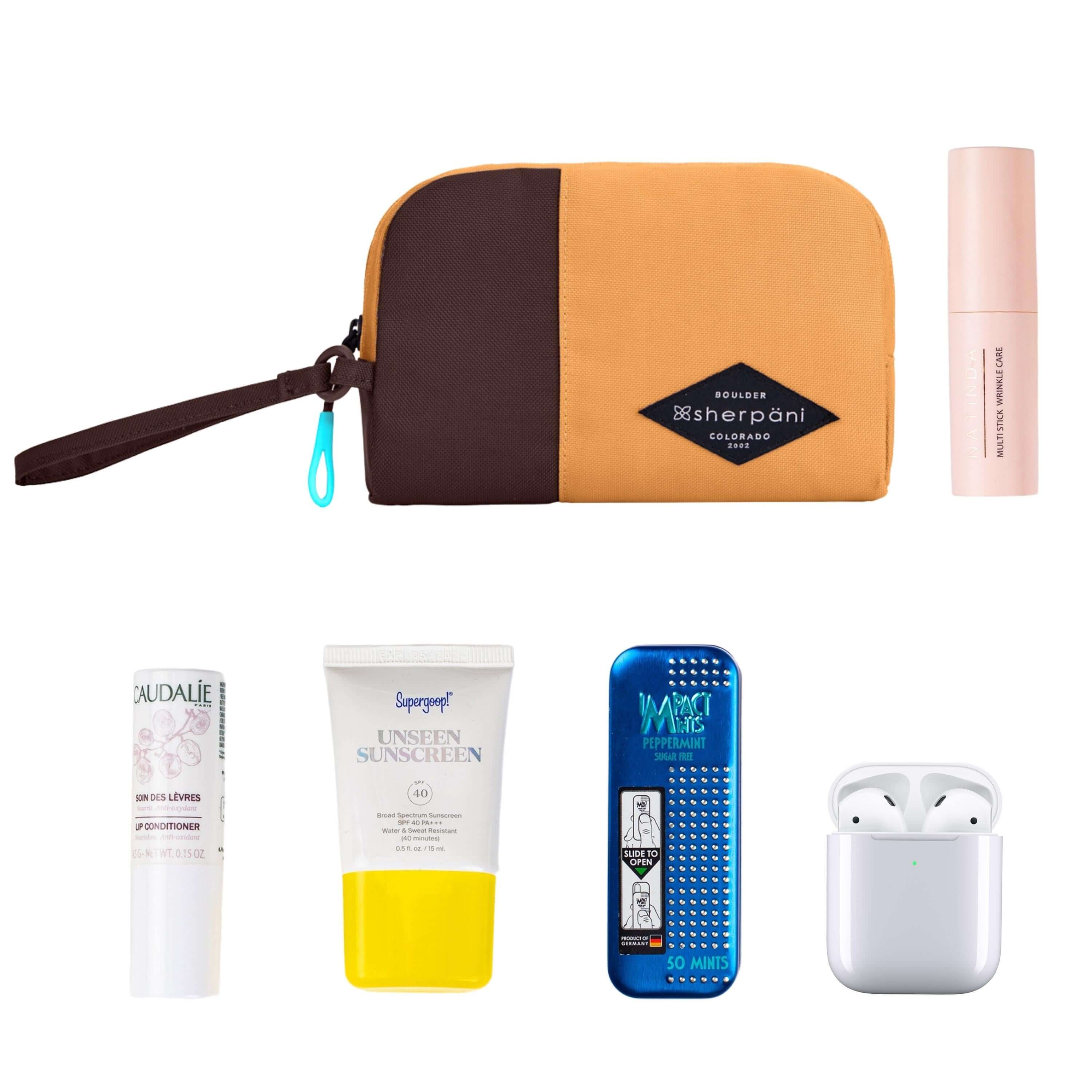 Top view of example items to fill the bag. Sherpani travel accessory, the Jolie in Sundial in small size, lies in the upper left corner. It is surrounded by an assortment of items: beauty product, skincare product, sunscreen, mints and AirPods.