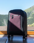Sherpani soft-shell carry-on luggage, the Latitude in Merlot, sits in front of a window looking out over a scenic mountain view.