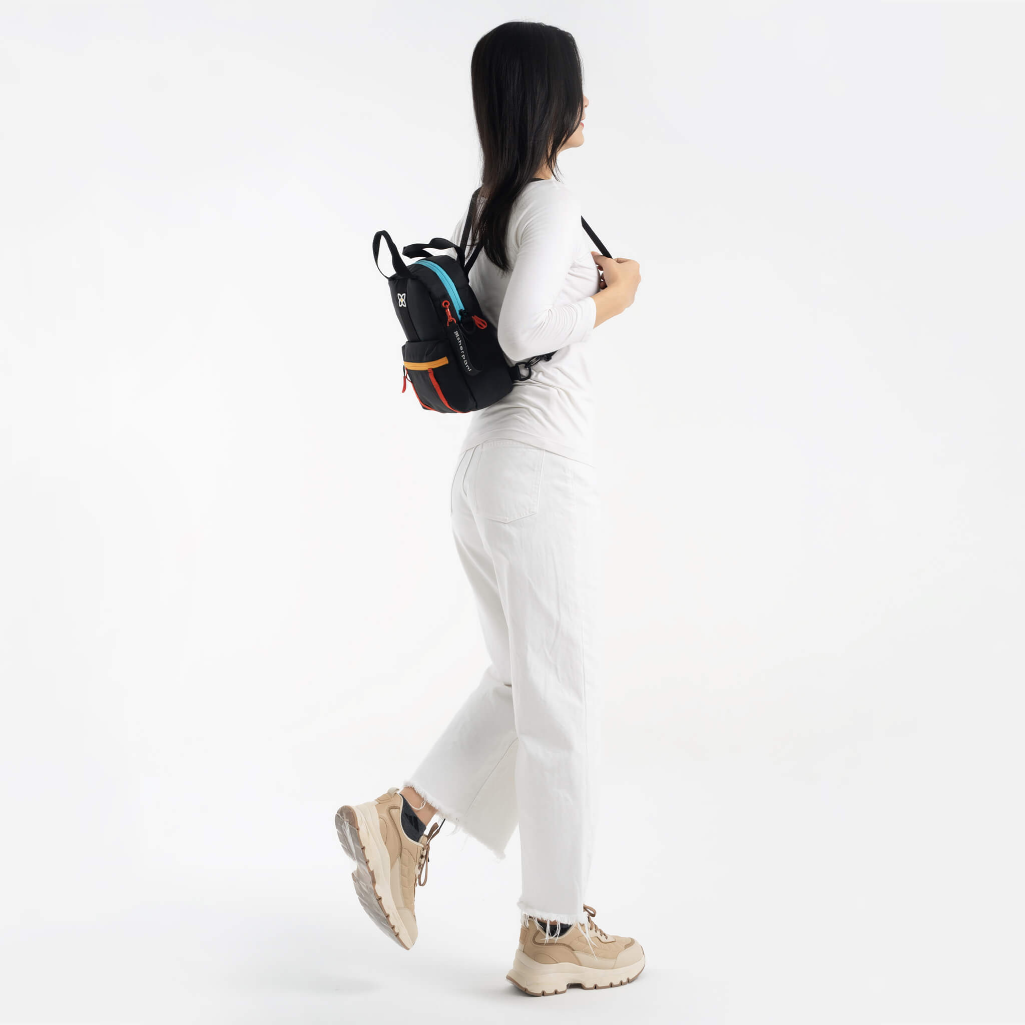 A model facing to the side. She is wearing a white top, white pants and the Logan mini backpack in Chromatic. 