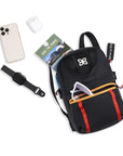 Top view of example items to fill the bag. Sherpani Logan mini backpack in Chromatic lies next to the following items: smart watch, headphones, sunglasses, hiking guide and phone.
