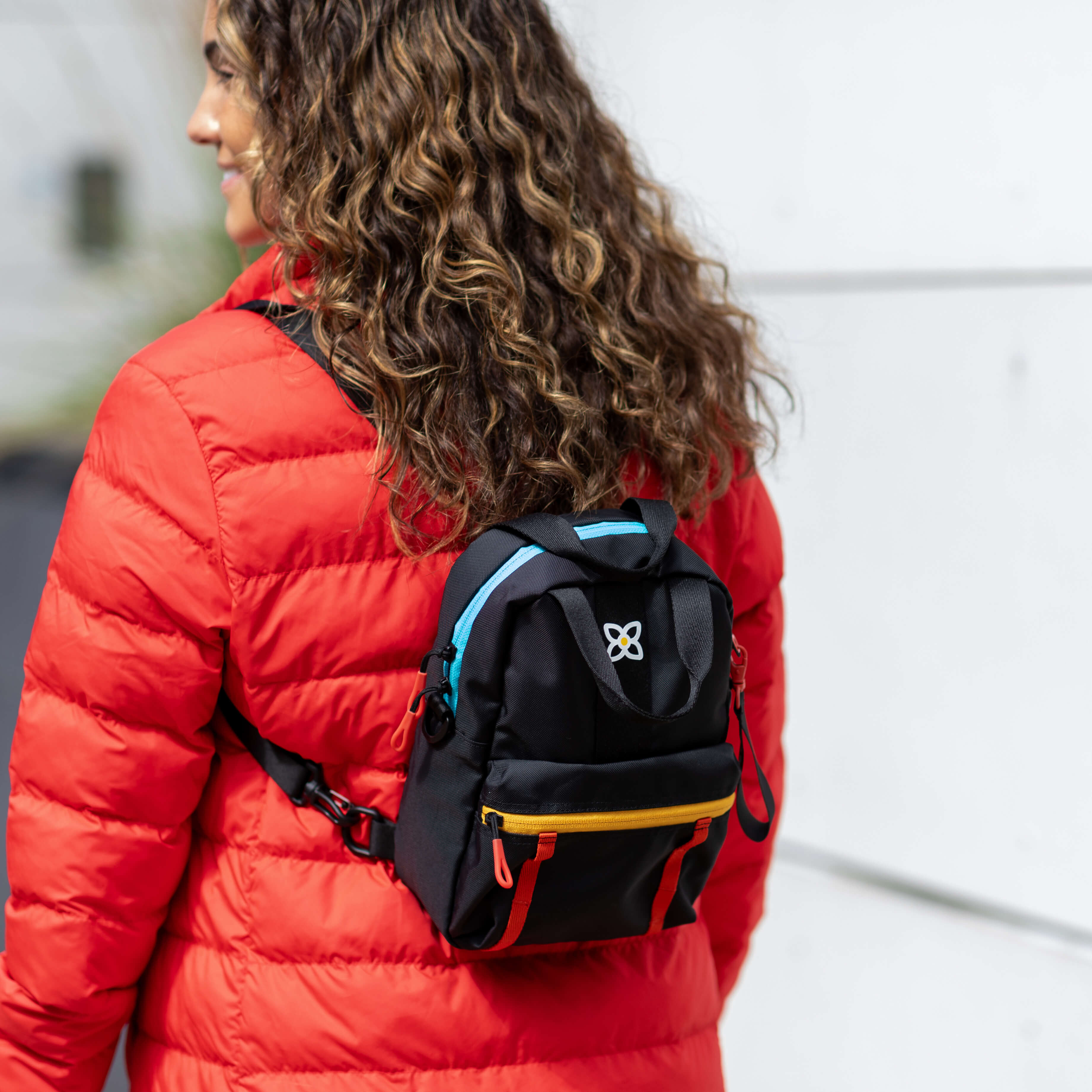 A woman stands outside. She is wearing Sherpani travel backpack, the Logan in Chromatic. #color_chromatic