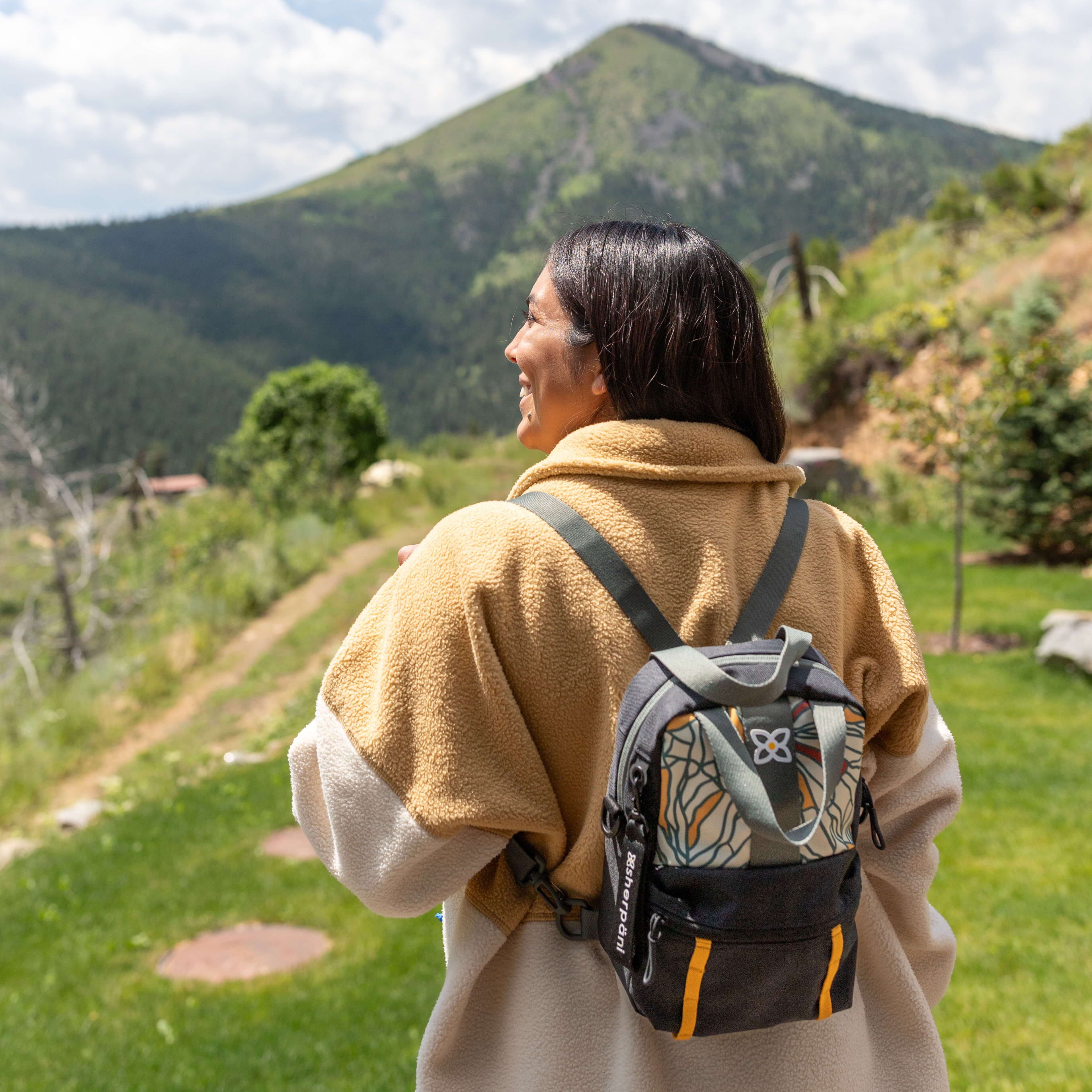 A woman stands outside in a scenic place. She is wearing Sherpani mini travel backpack, the Logan in Fiori. 