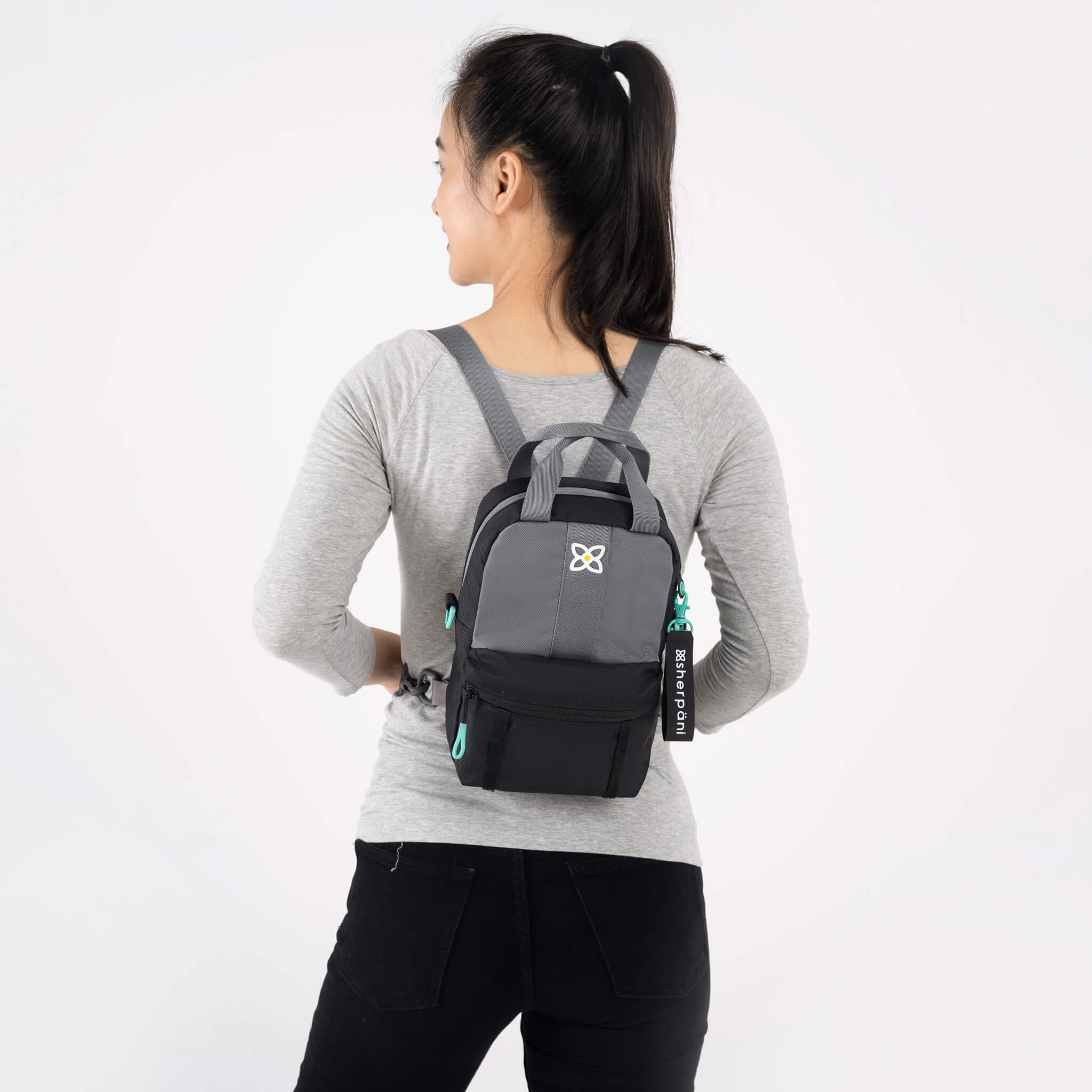 A model facing to the back. She is wearing a gray top, black leggings and the Logan mini backpack in Moonstone. 