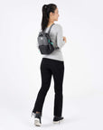 A model facing to the back. She is wearing a gray top, black leggings and the Logan mini backpack in Moonstone.