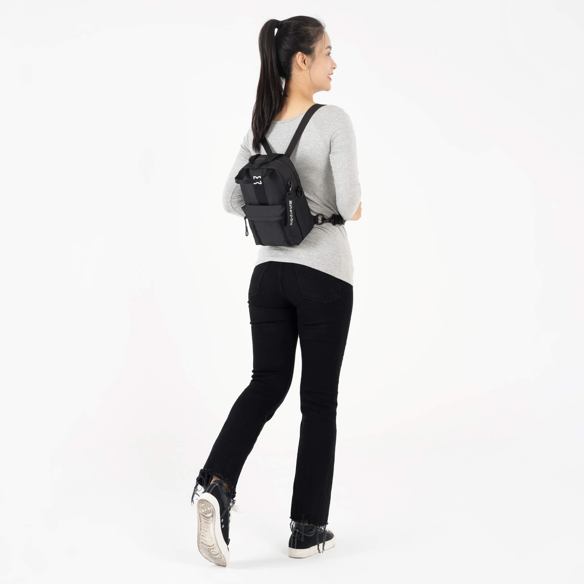 A model facing to the back. She is wearing a gray top, black leggings and the Logan mini backpack in Raven.