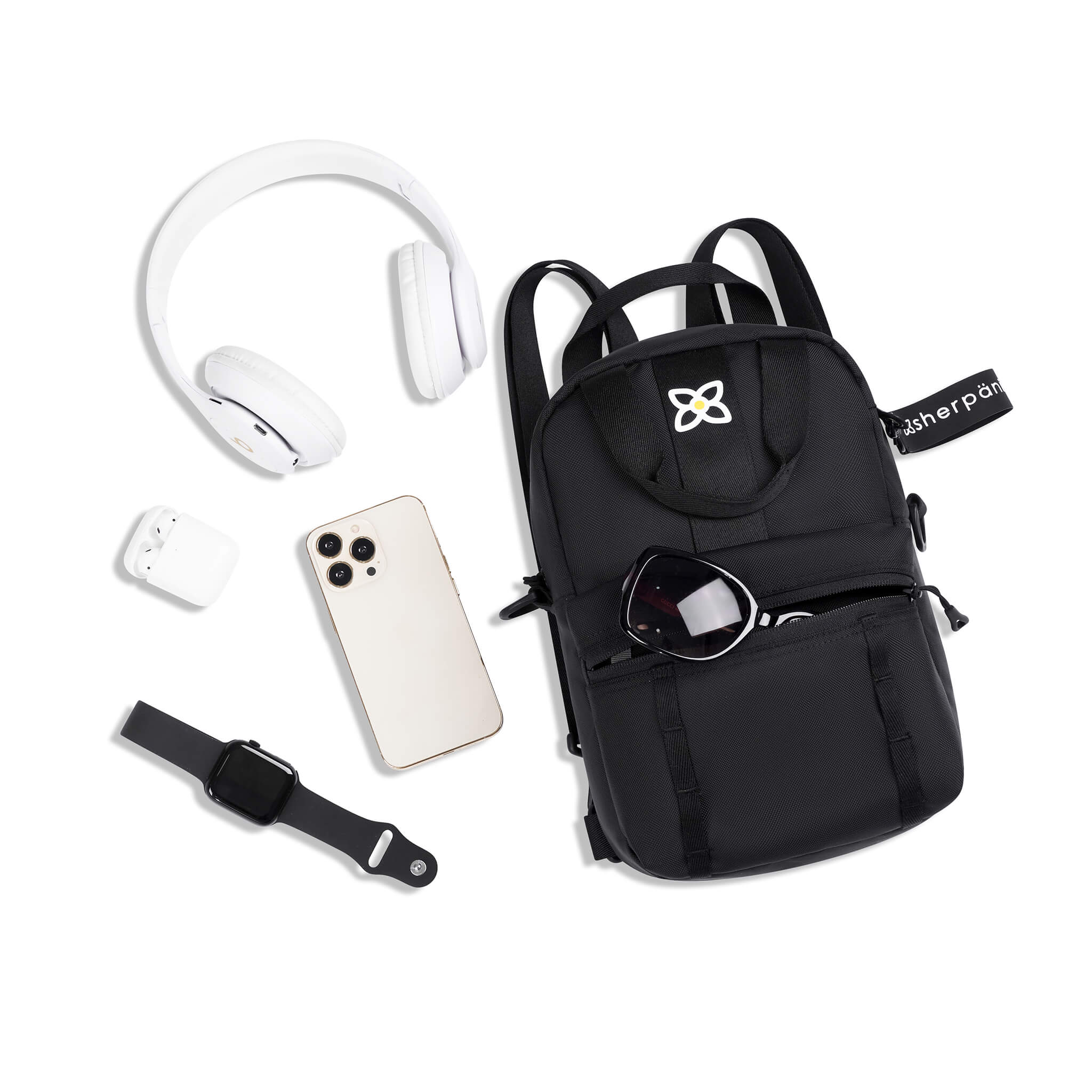 Top view of example items to fill the bag. Sherpani Logan mini backpack in Raven lies next to the following items: headphones, AirPods, phone, smartwatch and sunglasses. 