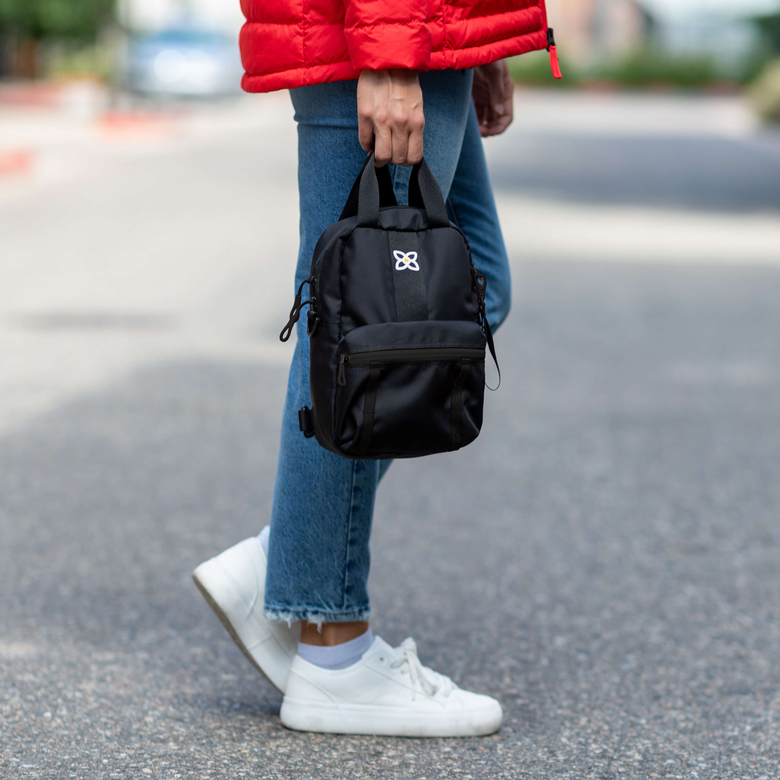 A woman carries Sherpani small backpack, the Logan in Raven, by the tote bag handles. 