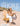 A woman sits on a wooden Adirondack chair on a sandy beach, wearing a white dress and sandals and holding a patterned Crossbodies handbag. Large white text at the top reads 'CARRY A SHORE THING' and smaller text at the bottom reads 'SHOP CROSSBODIES'.