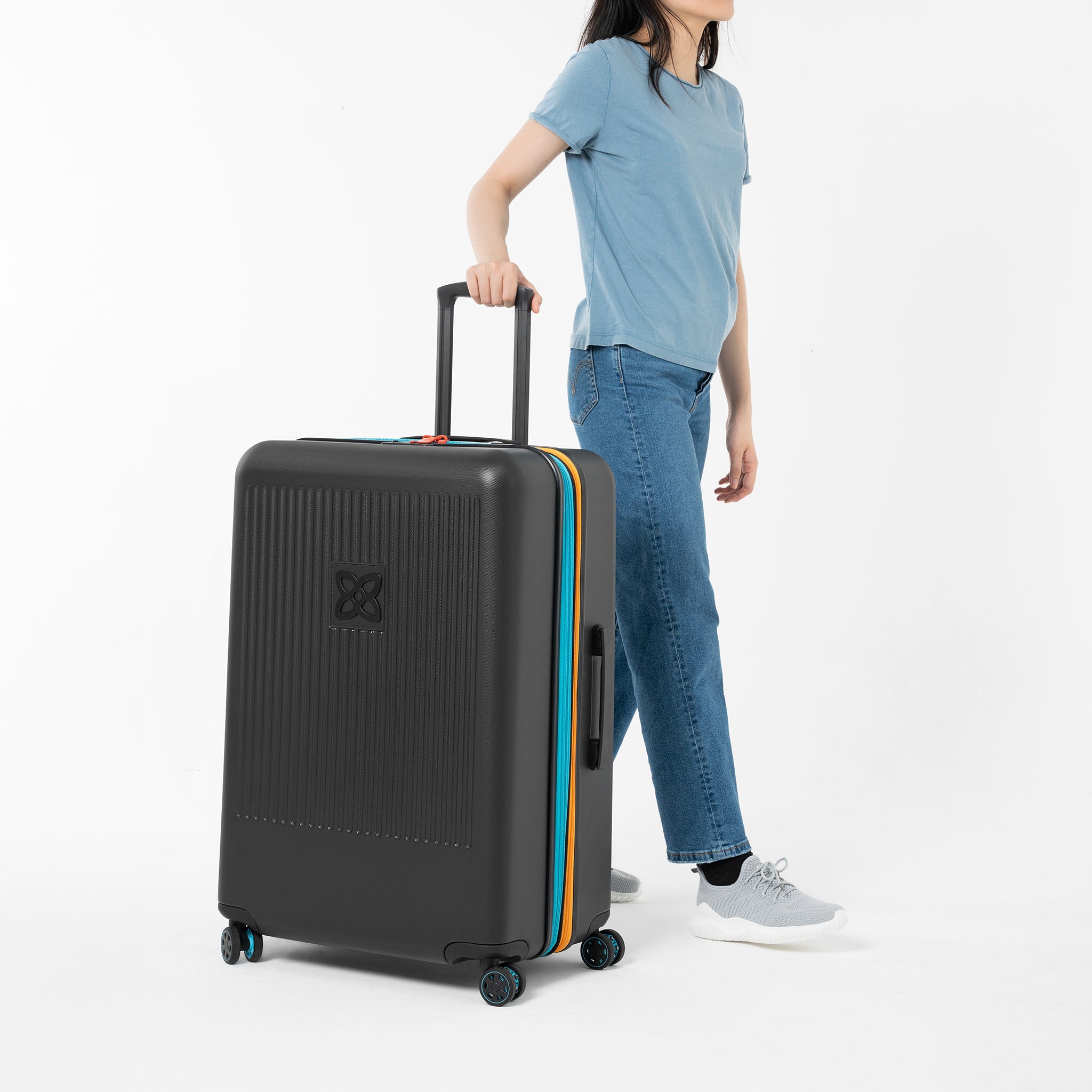 A model stands with one hand on the suitcase handle of Sherpani hard-shell luggage, the Meridian in Chromatic. 