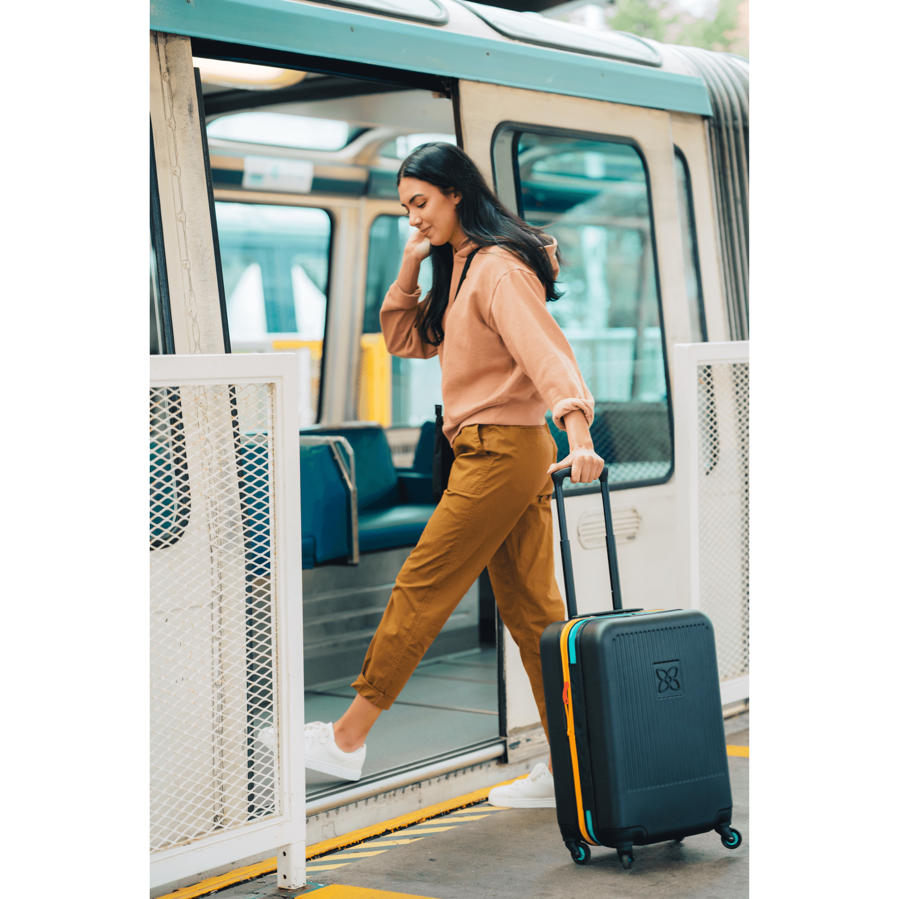 A woman stepping onto a train with Sherpani hard shell luggage, the Meridian. Part of Sherpani travel Carry on Bundle in Cool Chromatic. 