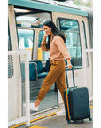 A woman stepping onto a train with Sherpani hard-shell luggage, the Meridian. Part of Sherpani travel Carry-on Bundle in Cool Chromatic.