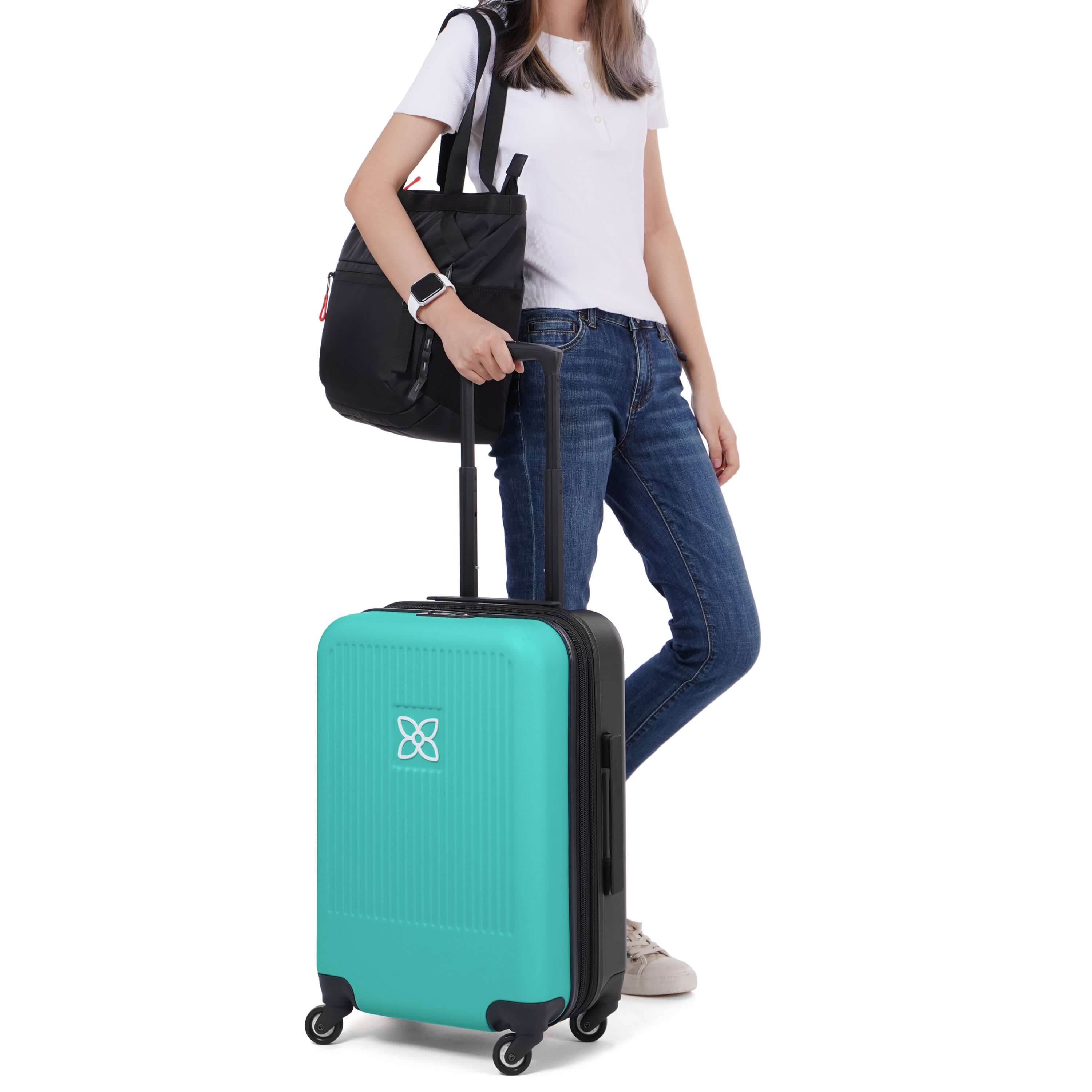 A model stands with one hand on the suitcase handle of Sherpani hard-shell carry-on suitcase, the Meridian in Caribe. Over her shoulder is Sherpani travel bag, the Stride in Raven. 