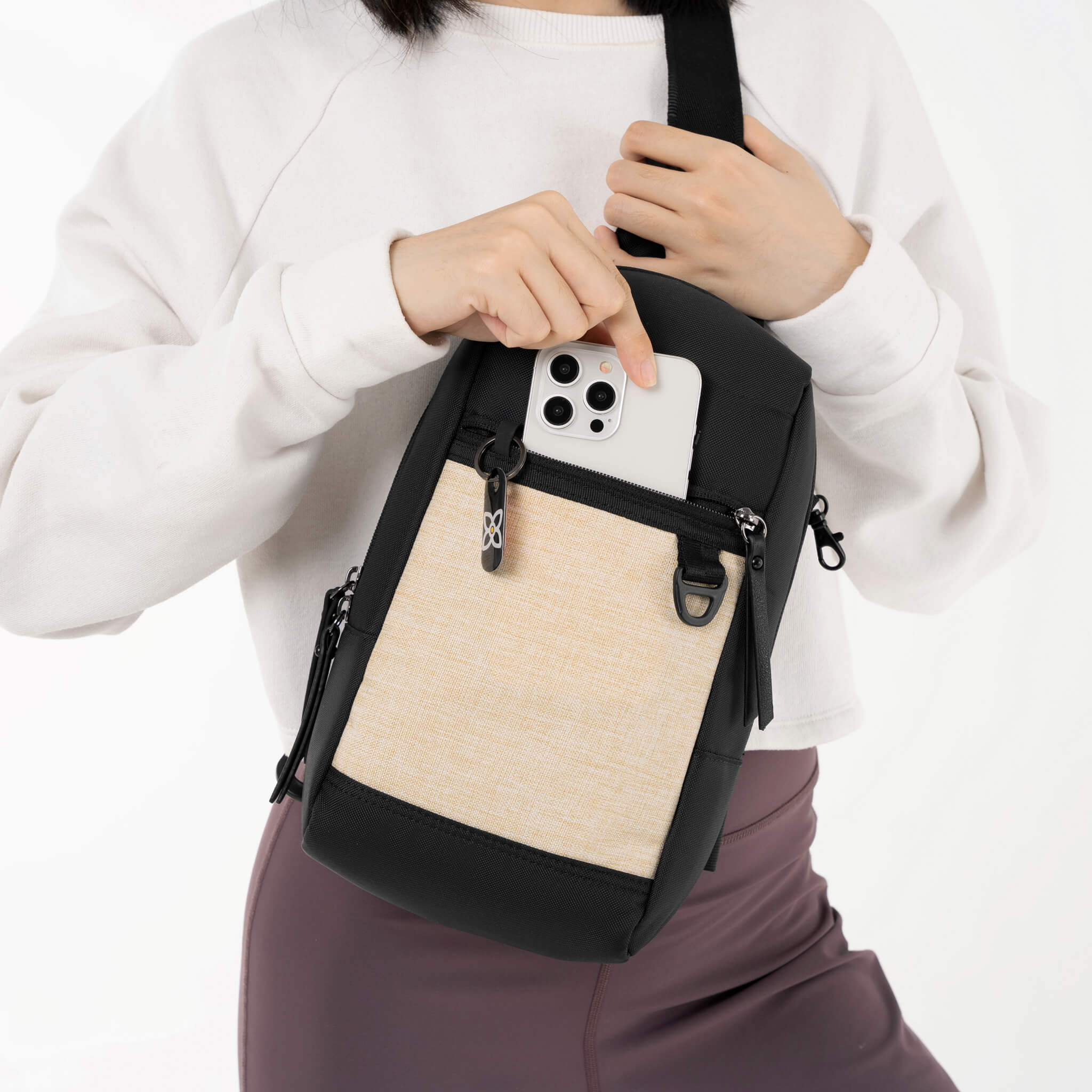 A model pulling her phone out of the lockable zipper pocket on Sherpani mini sling bag, the Metro in Straw. 